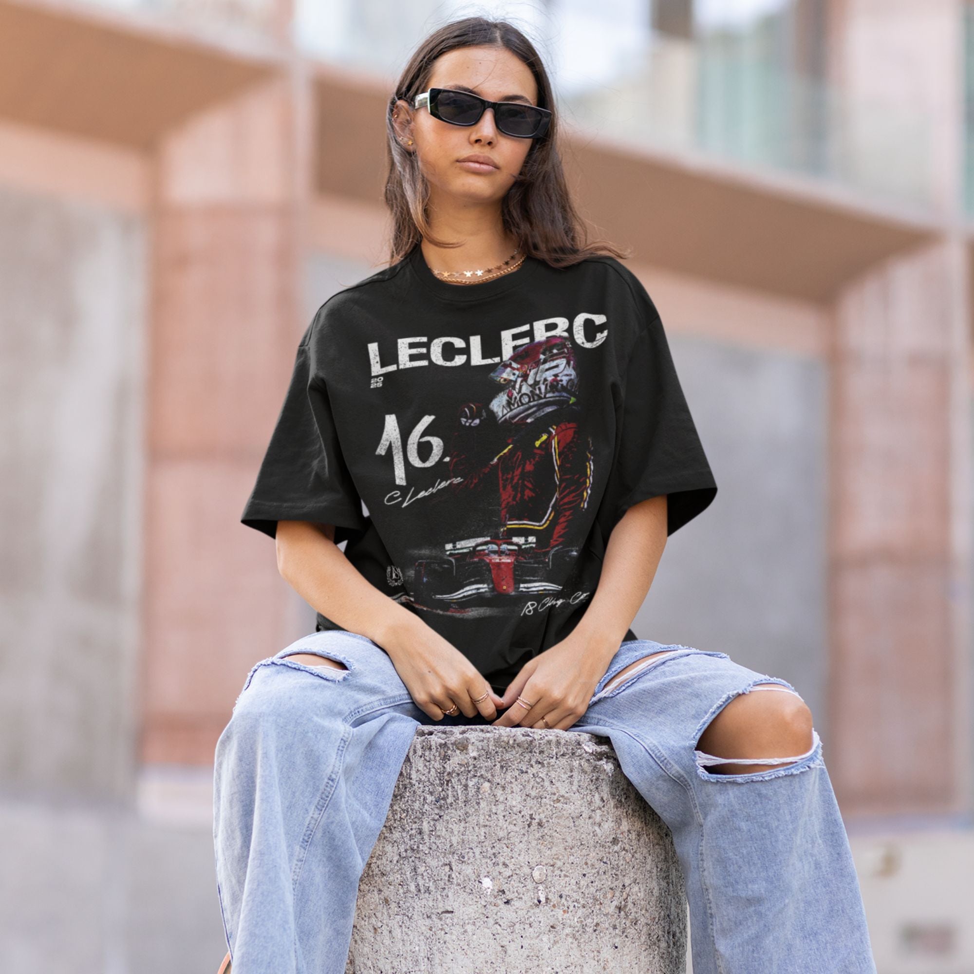 Person wearing a black t-shirt with graphics and text, sitting on a concrete block.