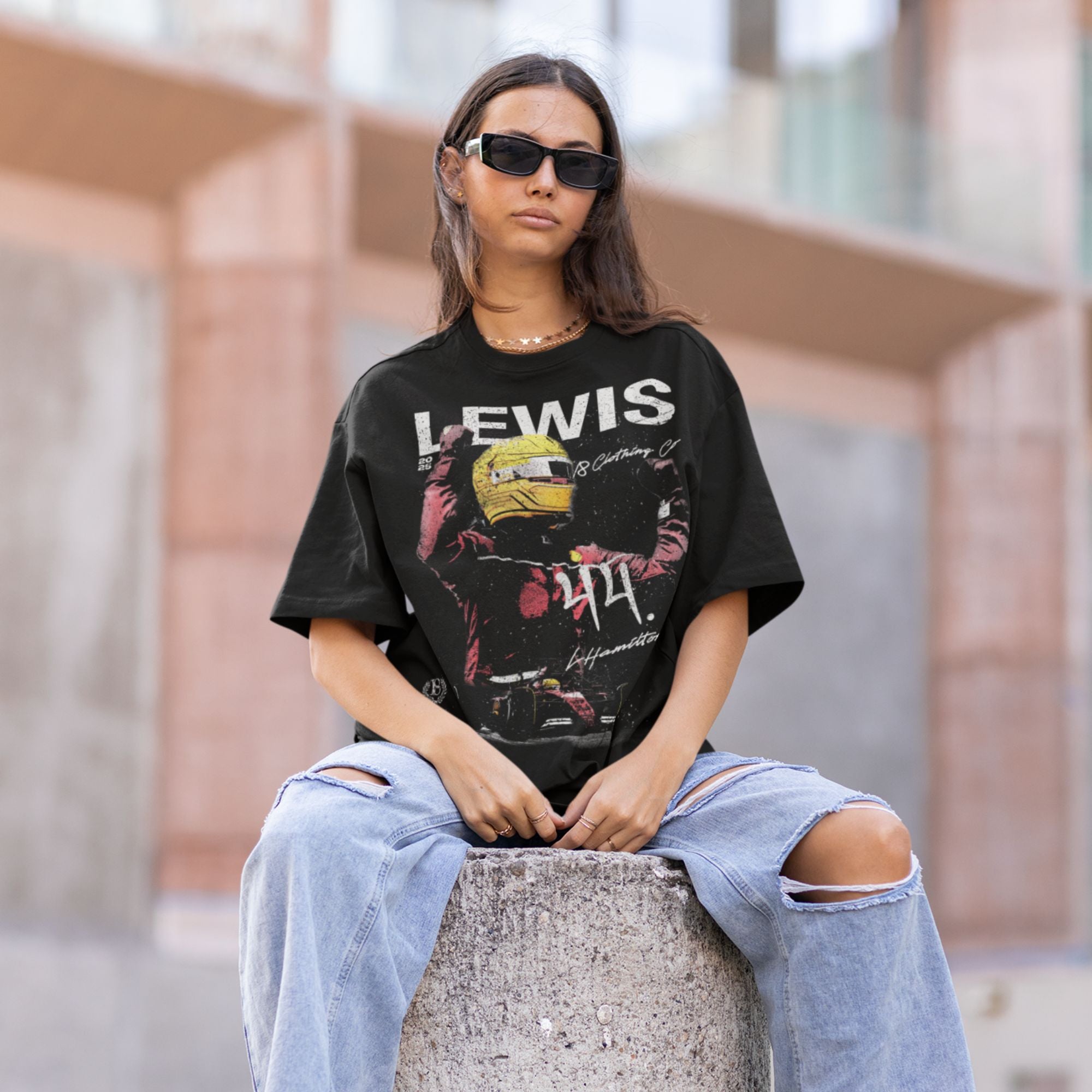Person wearing a black t-shirt with 'LEWIS' graphic design, sitting on a concrete block.