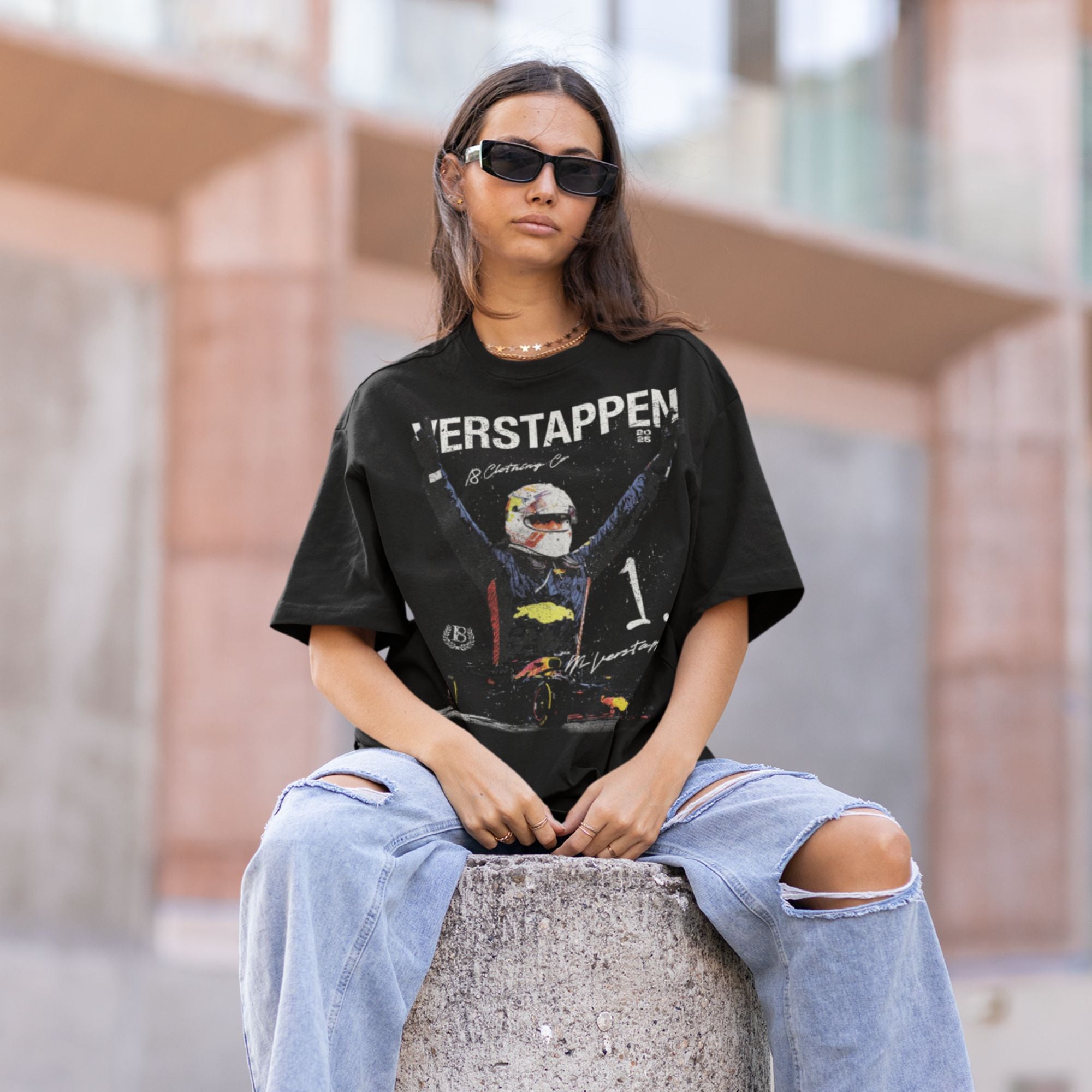 Person wearing a black graphic t-shirt and ripped jeans sitting on a concrete block.