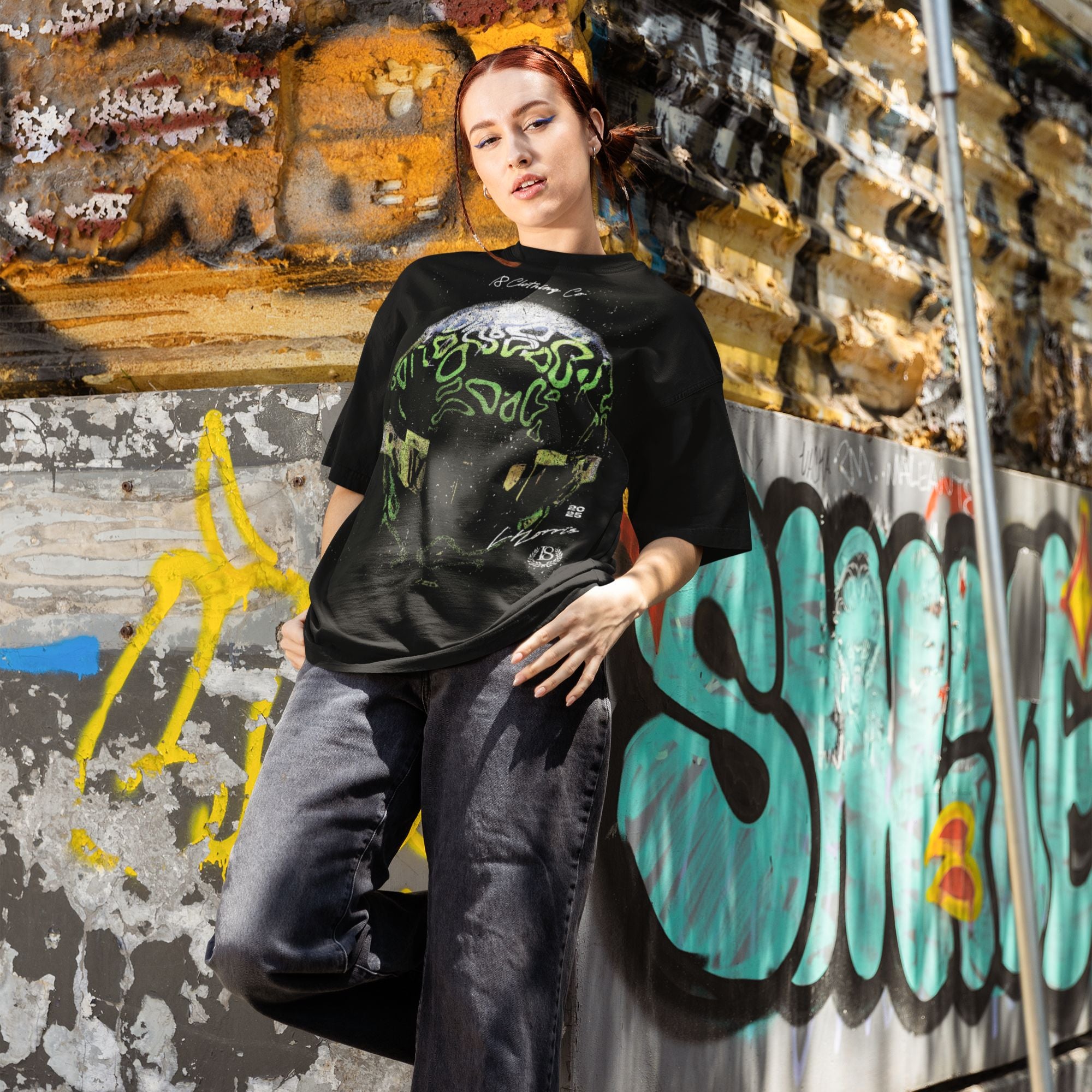 Person wearing a black t-shirt with green graphics against a graffiti-covered wall.