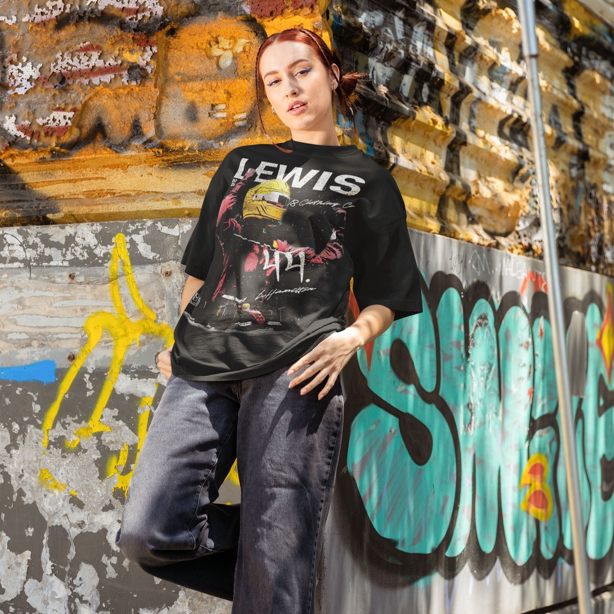 Person wearing a black t-shirt with graphic design and text, standing in front of a graffiti-covered wall.