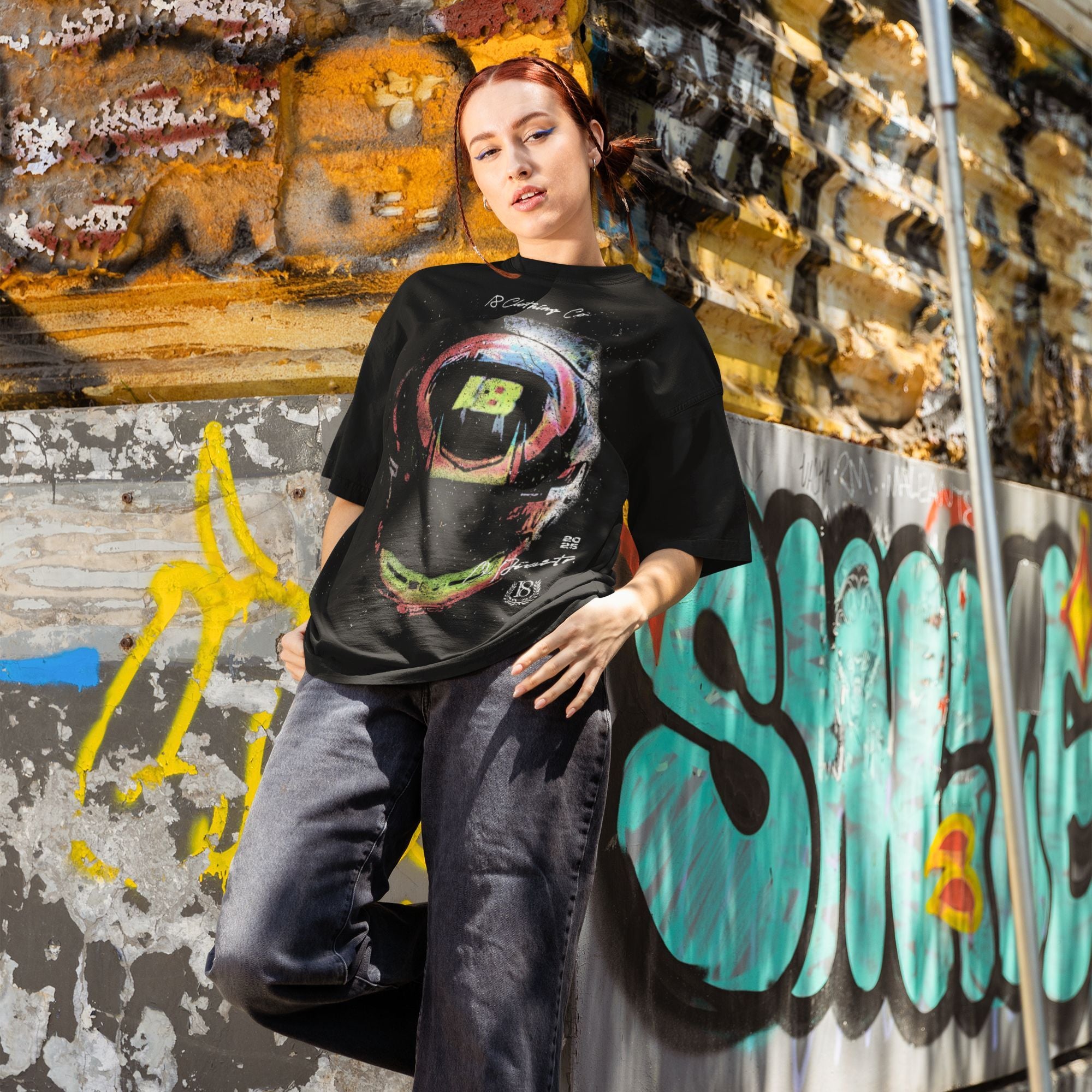 Person wearing a black t-shirt with a colorful graphic design in front of a graffiti-covered wall.