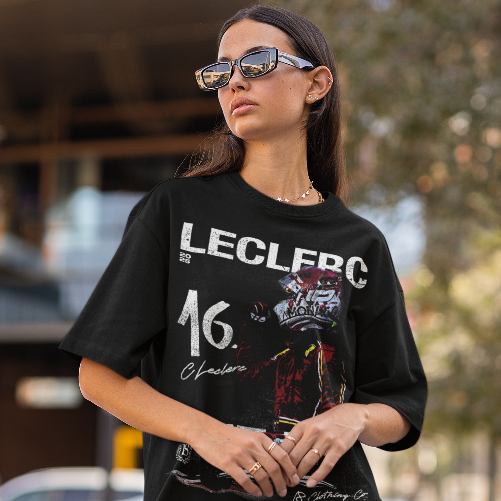 Woman wearing a black t-shirt with 'LECLERC' and number '16' printed on it, outdoors.