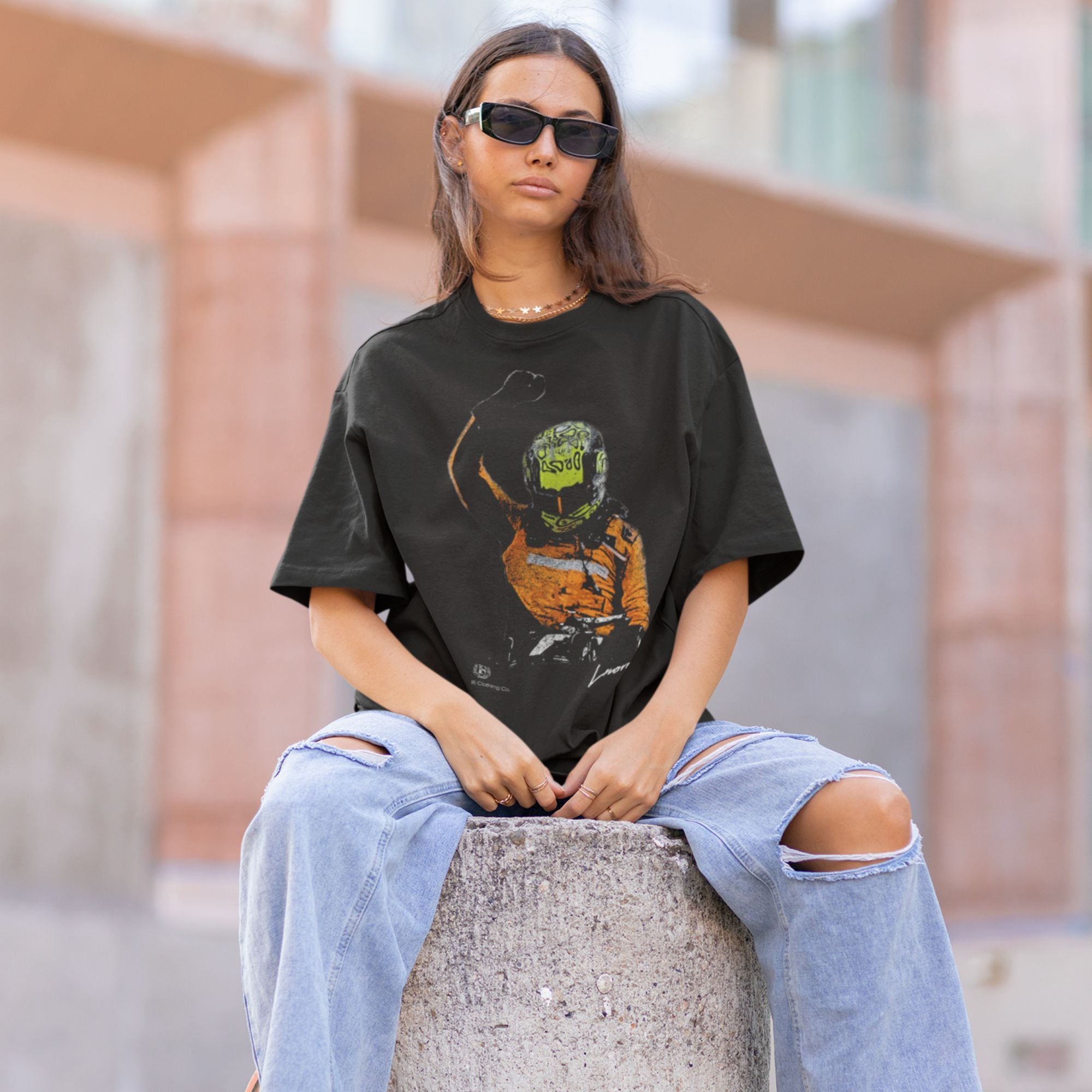 Person wearing a black t-shirt with a graphic design and ripped jeans sitting on a concrete block.