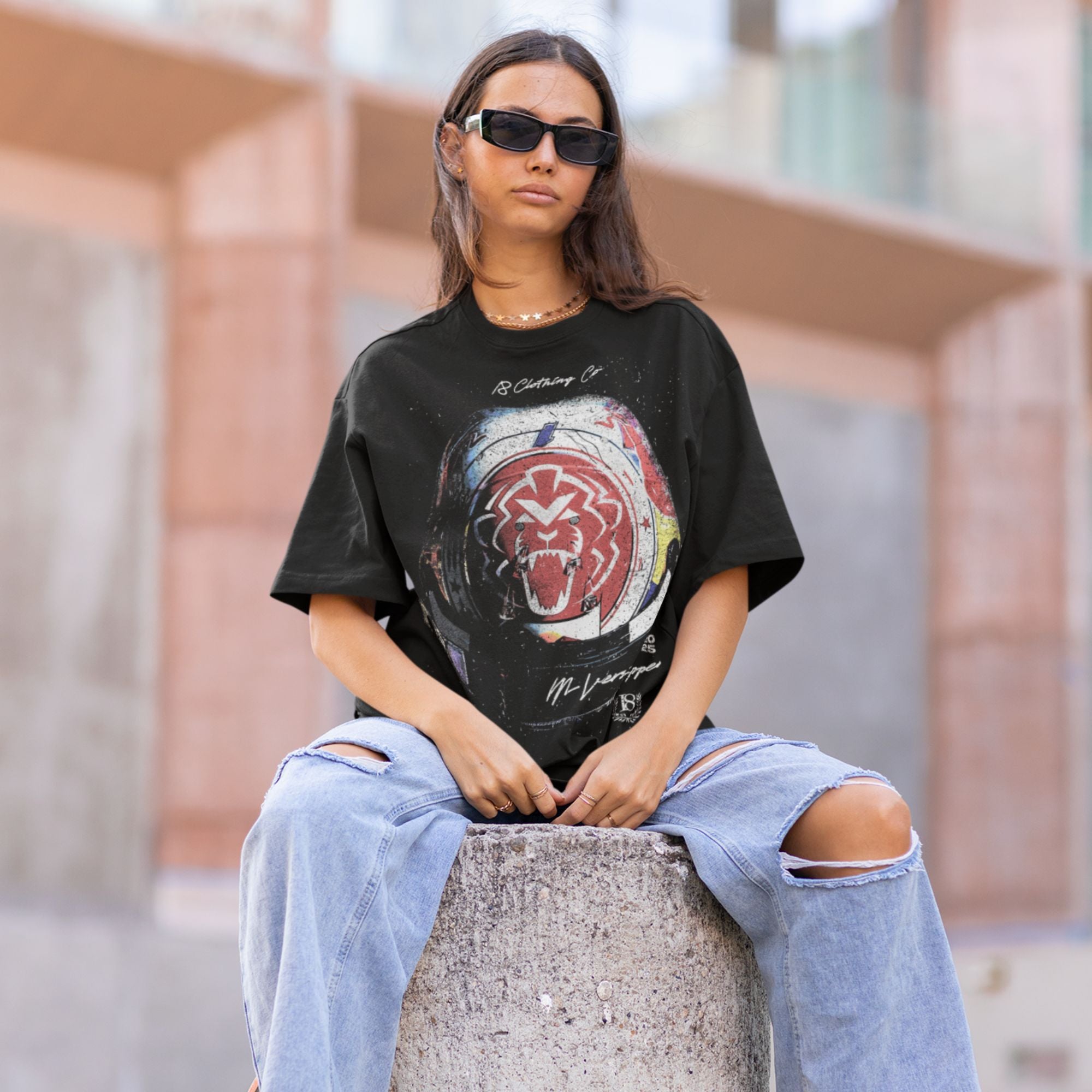 Person wearing a black graphic t-shirt and ripped jeans sitting on a concrete block.