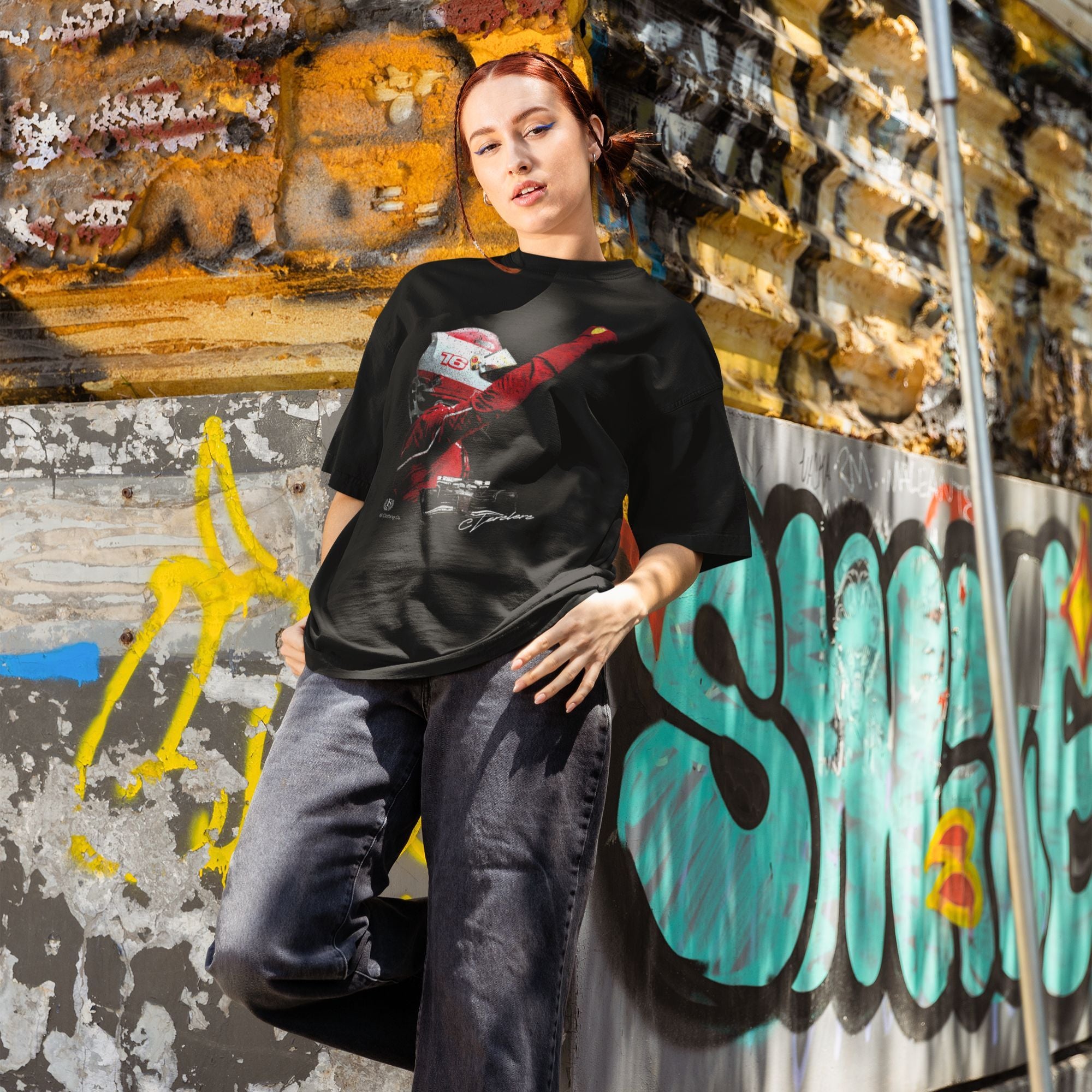 Person wearing a black t-shirt with a graphic design in front of a graffiti-covered wall.