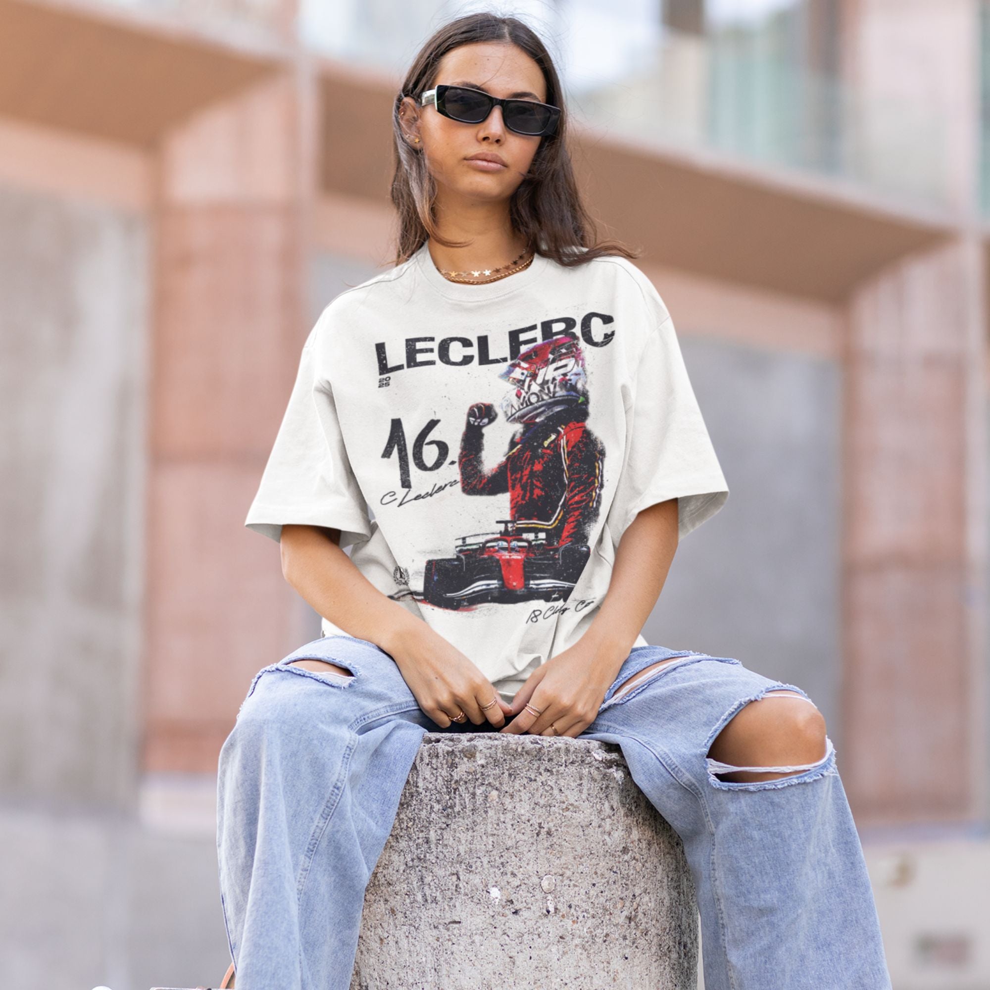 Person wearing a graphic t-shirt and ripped jeans sitting on a concrete block.