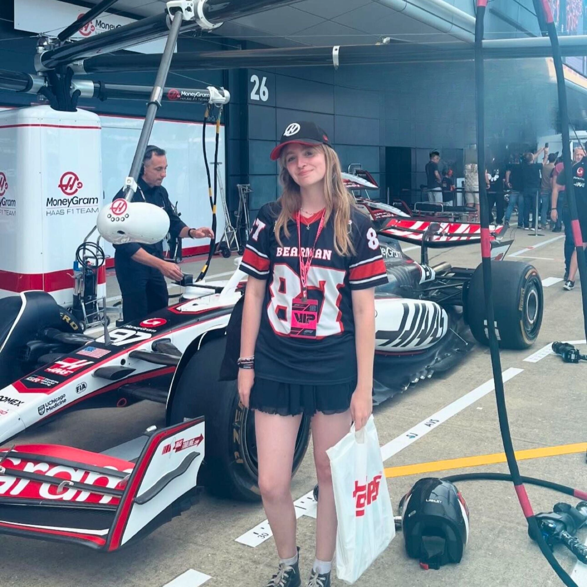 Person in a racing-themed outfit standing next to a Formula 1 car in a garage.