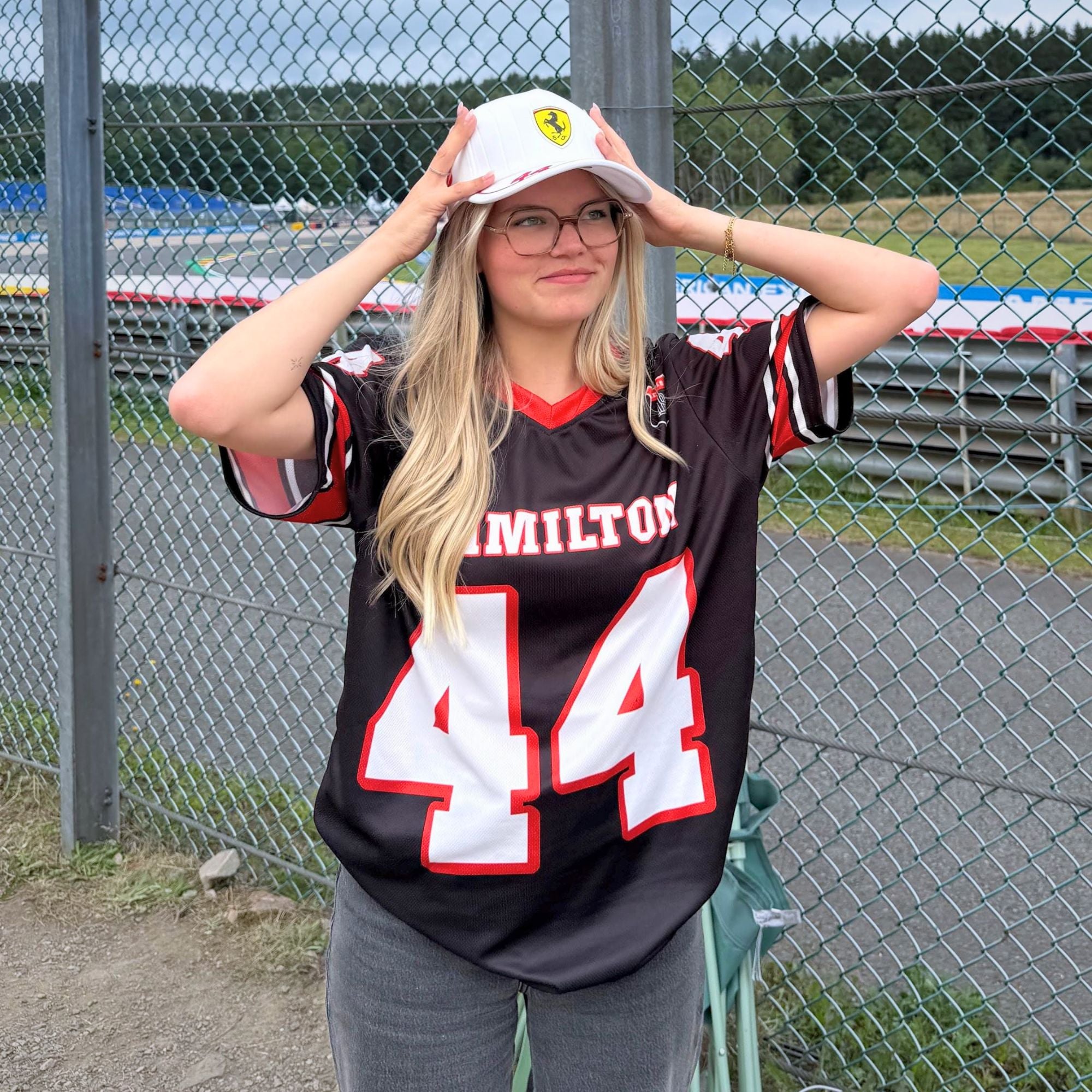 Person wearing a Hamilton 44 jersey and Ferrari cap in front of a fence.