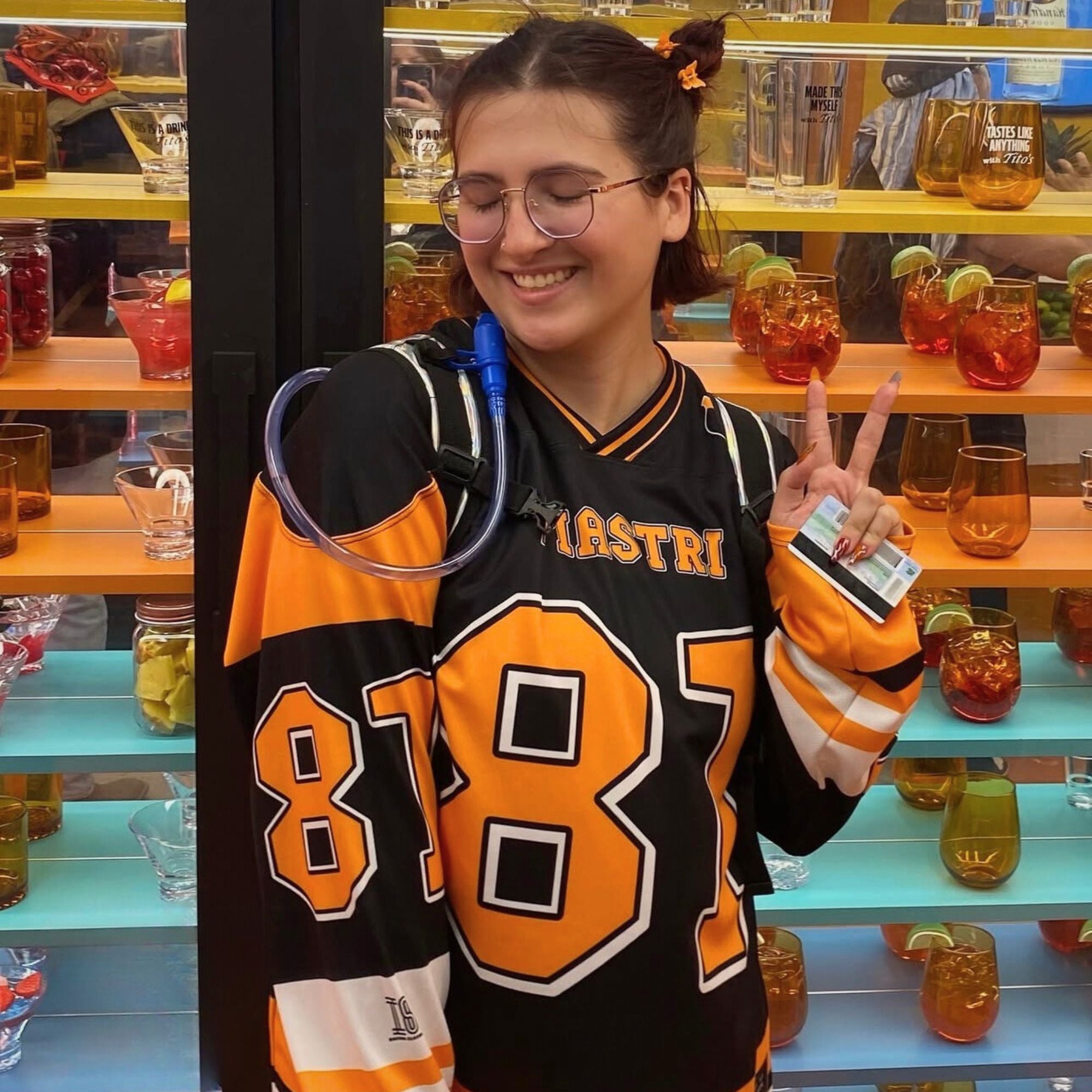 Person wearing a black and orange sports jersey with the number 81, standing in front of shelves with drinks.