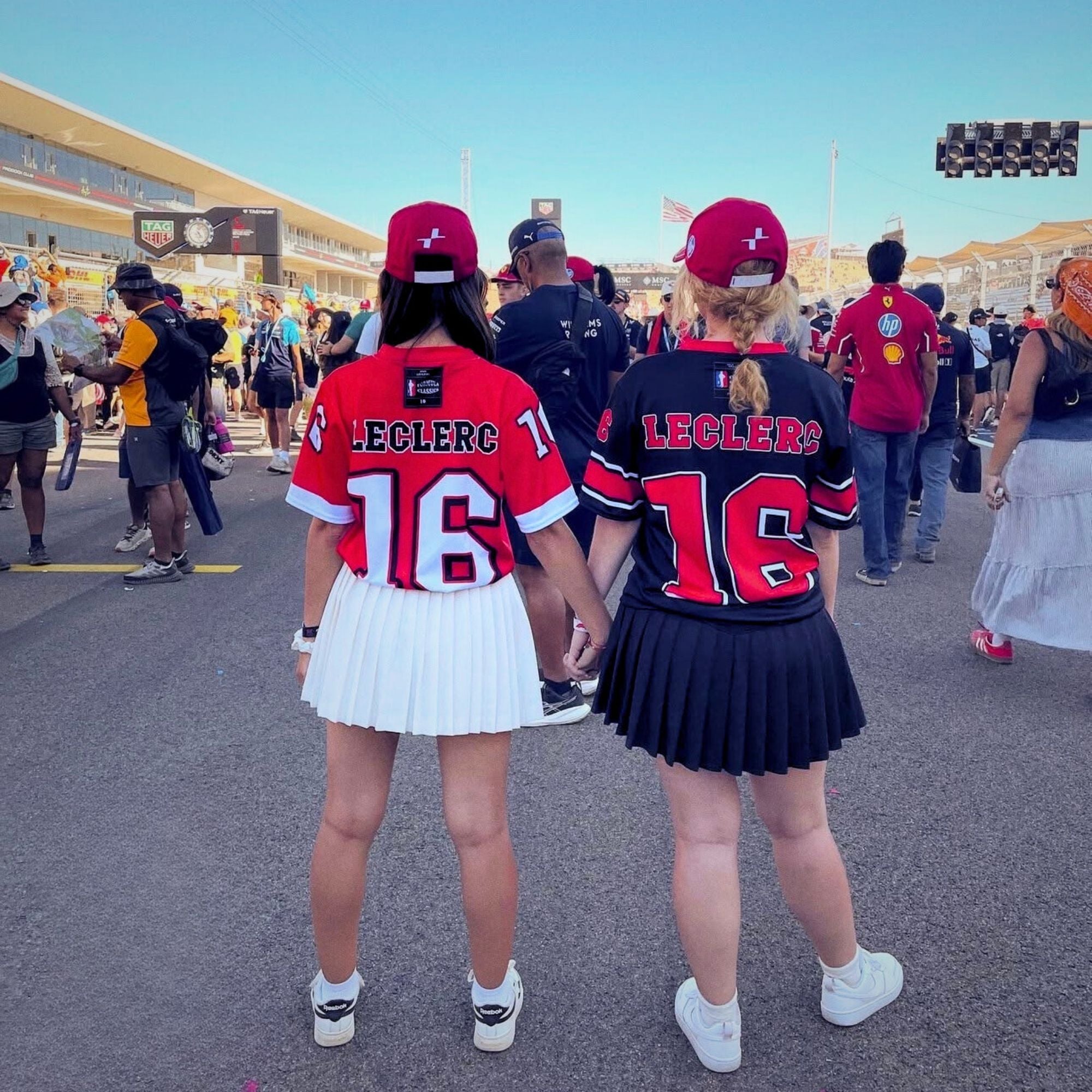 Two people wearing red and black sports jerseys with 'LECLERC' and number '16' at a sports event.