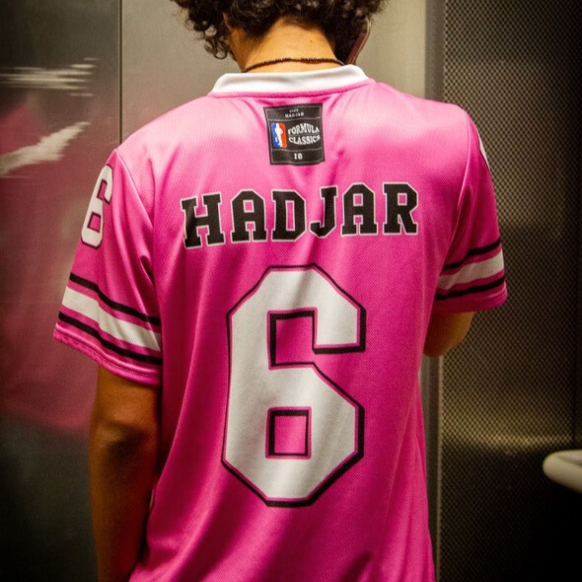 Person wearing a pink sports jersey with 'HADJAR' and number '6' in a locker room setting.