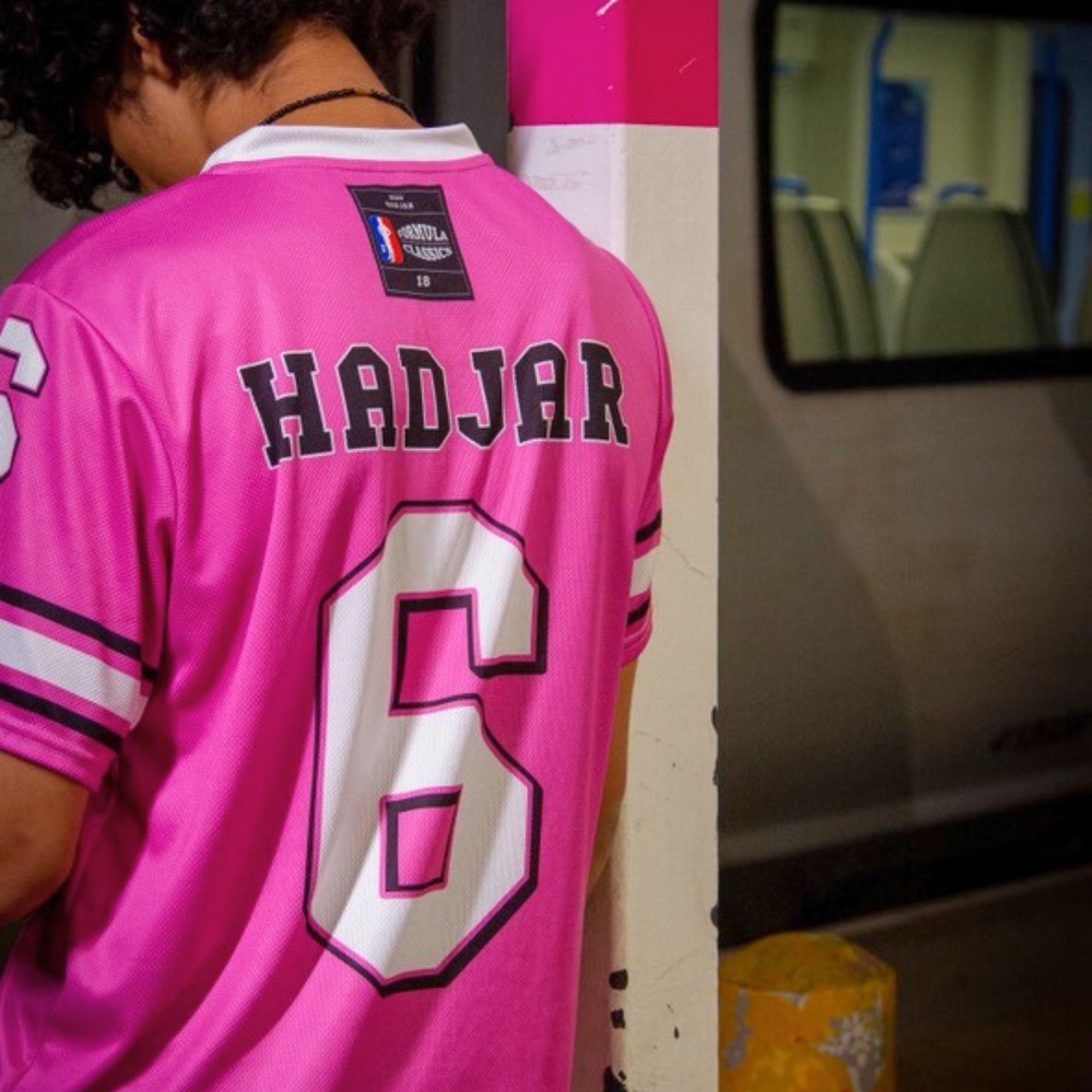 Person wearing a pink sports jersey with 'HADJAR' and number '6', standing next to a vehicle.