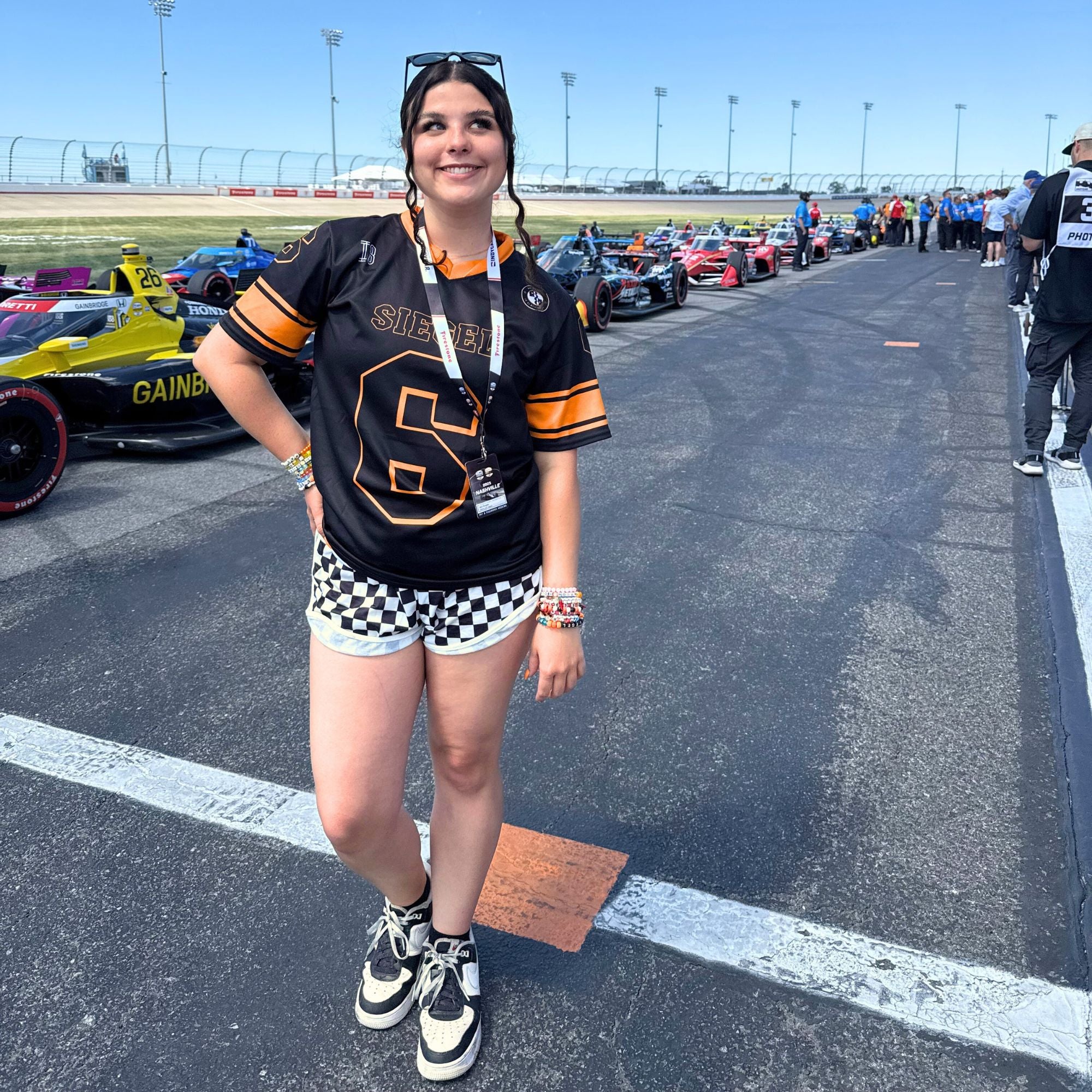 Person in a racing-themed outfit standing on a race track with racing cars in the background.