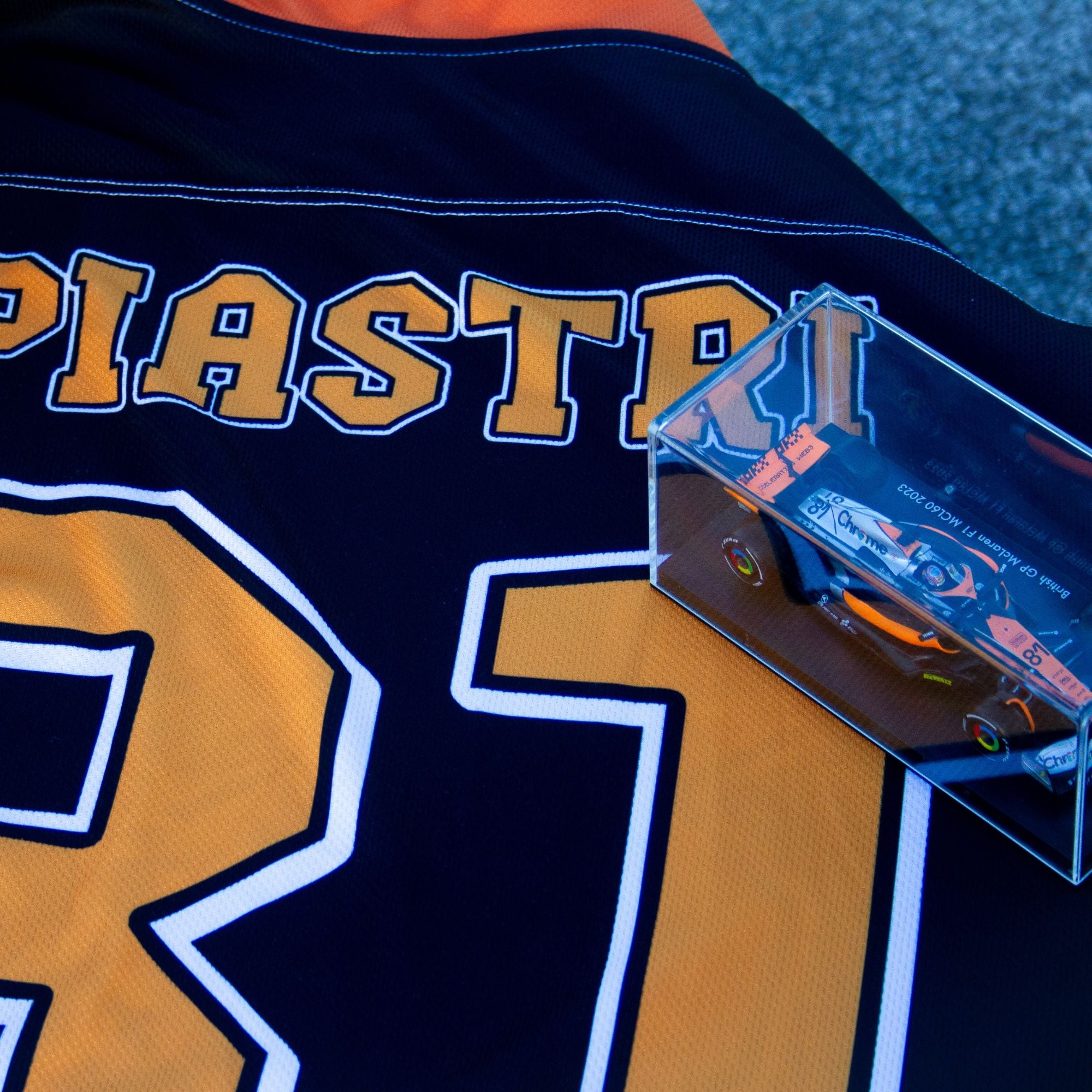 A black hockey jersey with Oscars piastri's McLaren F1 racing number 81 on the front and back in papaya orange, also the name Piastri is on the back in orange