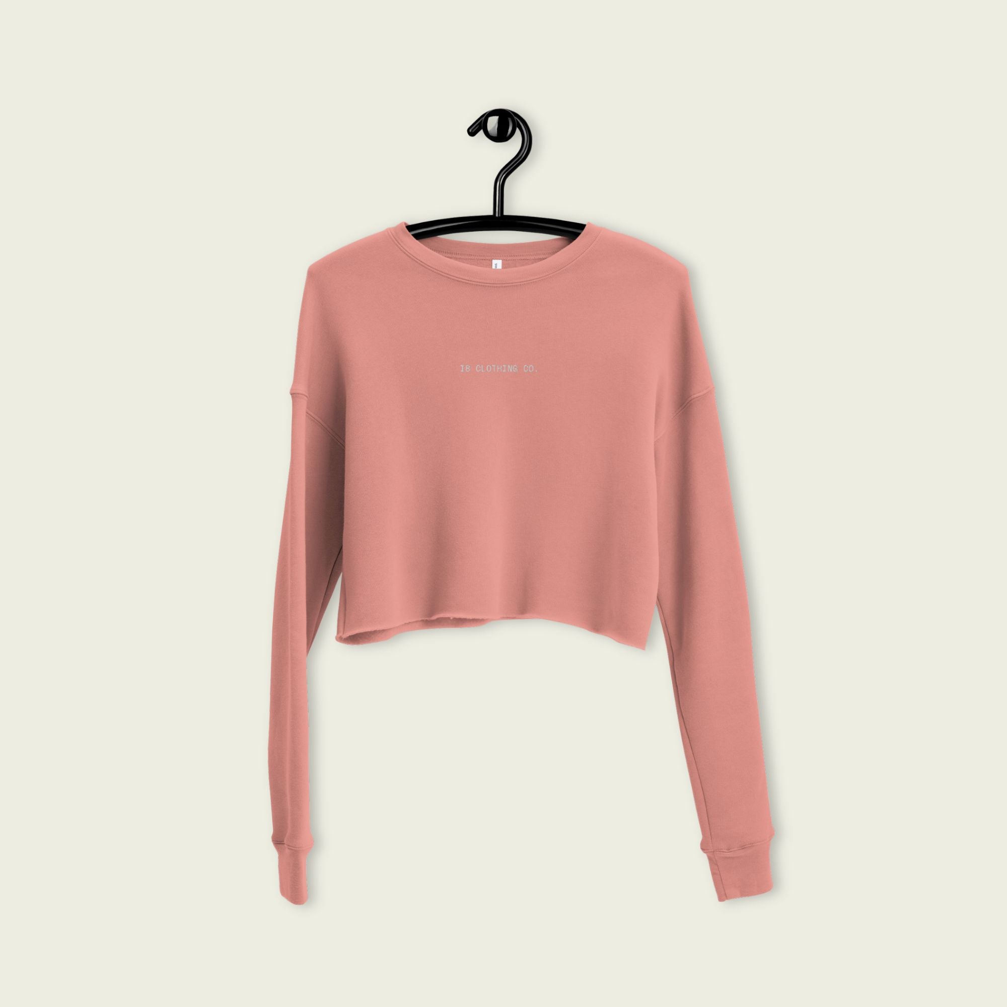 Pink long-sleeve crop top on a hanger against a beige background