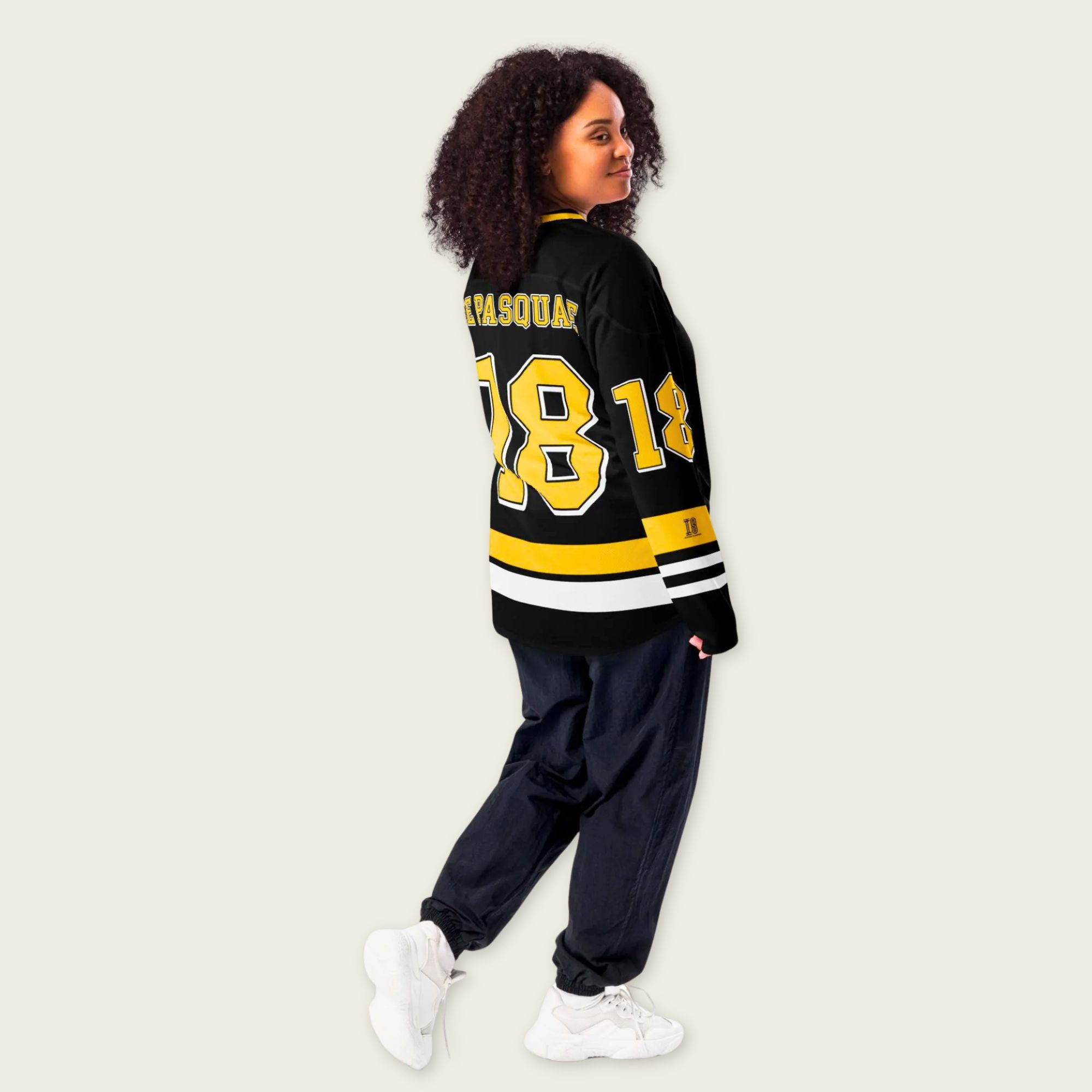 Person wearing a black and yellow varsity jacket with the number 18 on a beige background