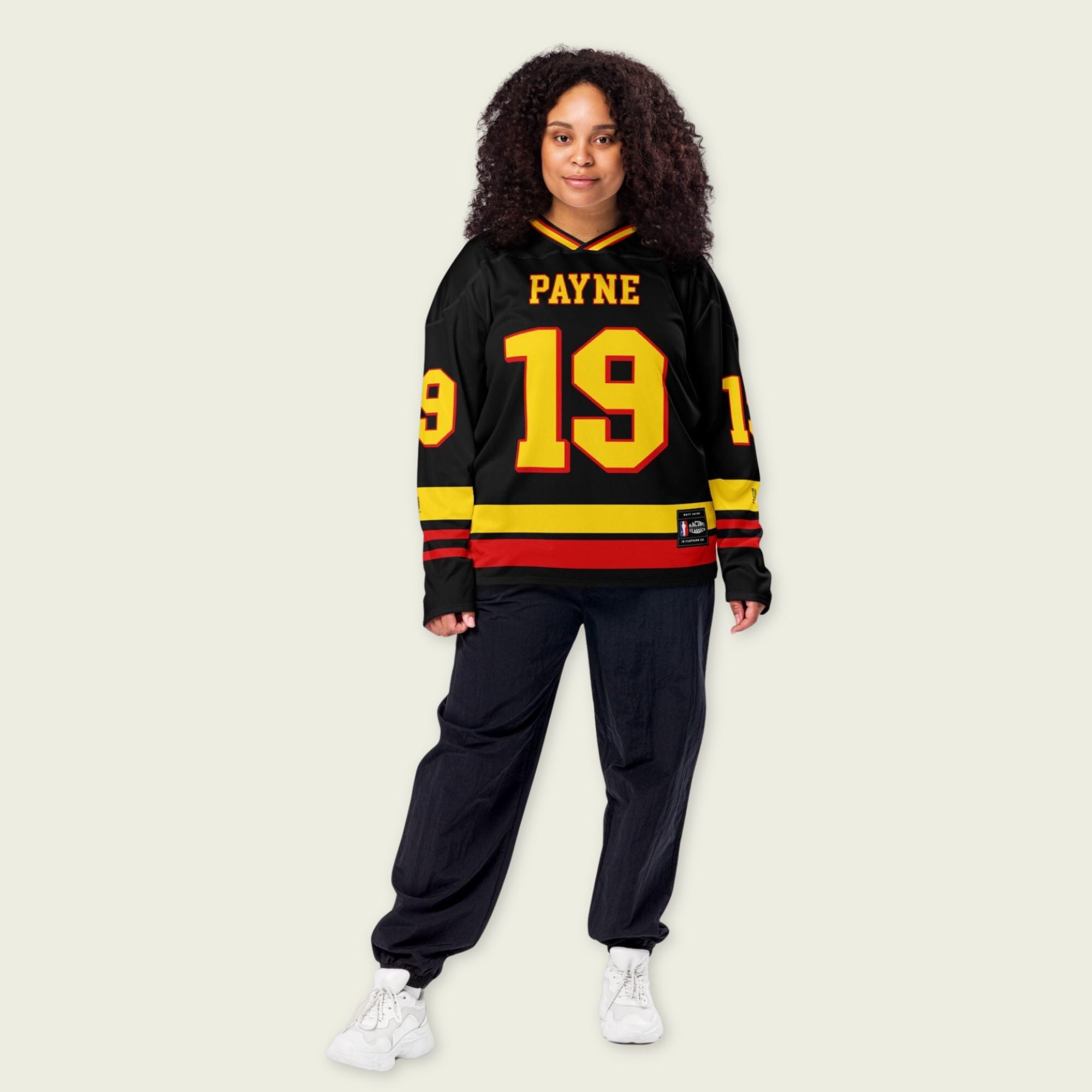 Person wearing a black sports jersey with yellow and red details on a beige background