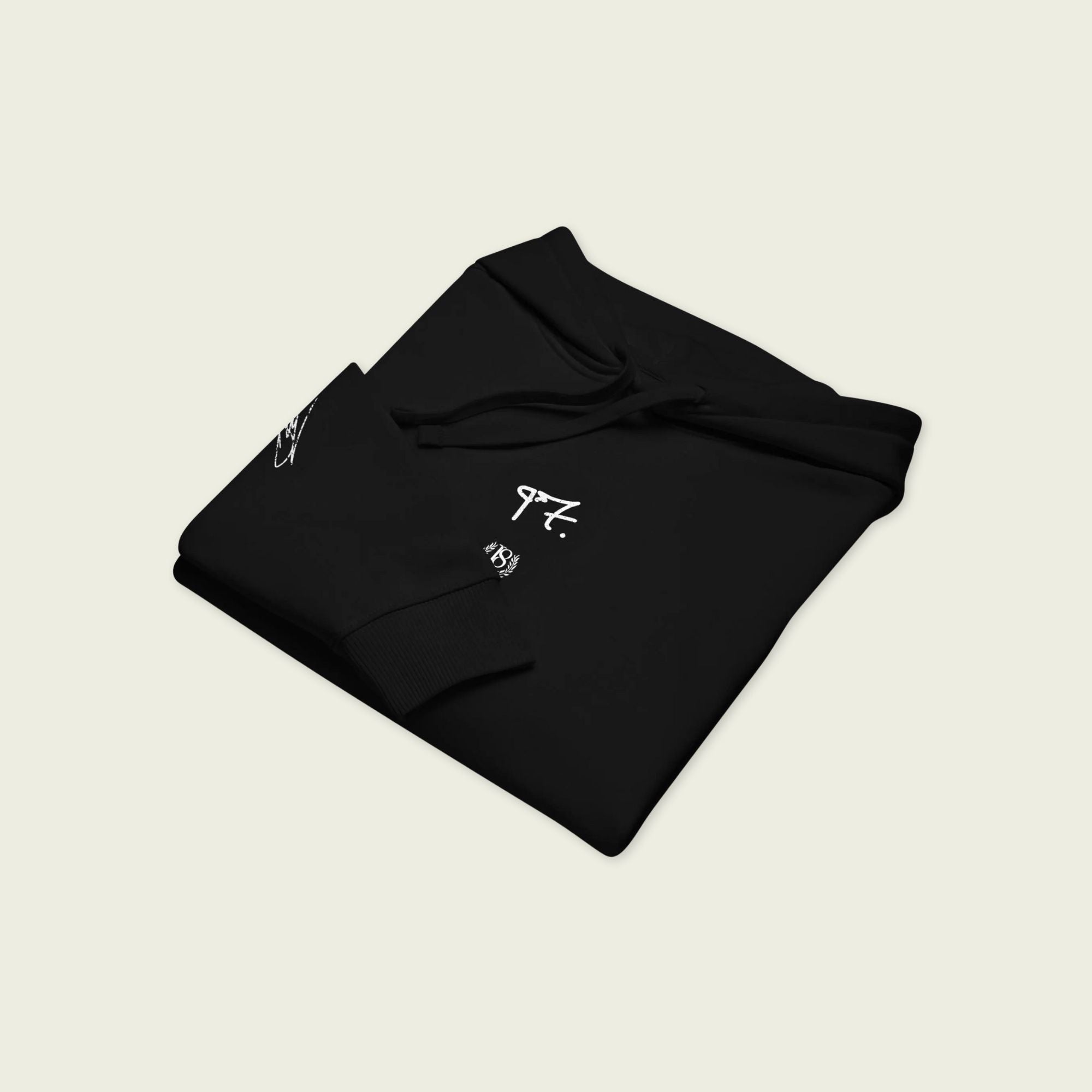 Folded black hoodie with white logos on a beige background
