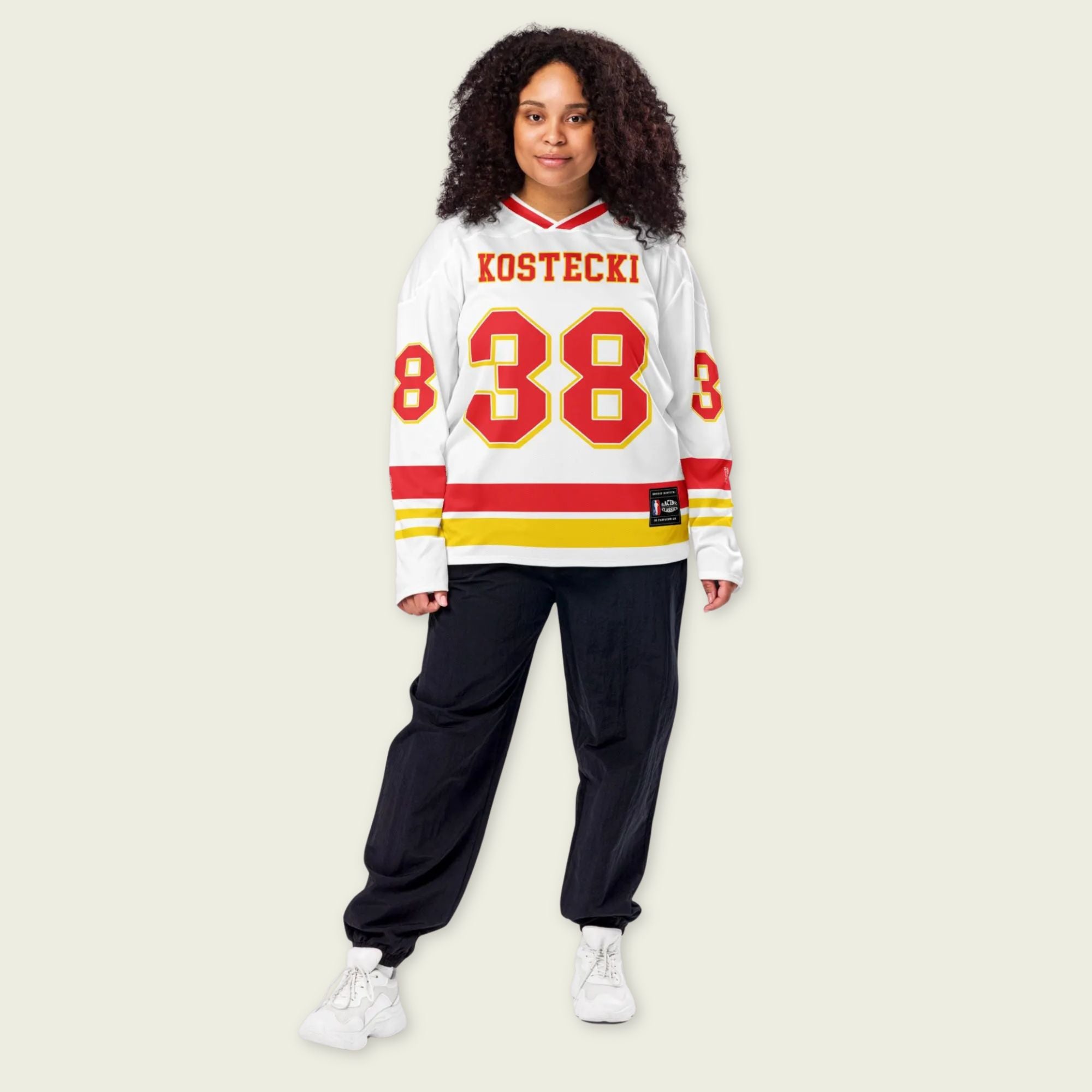 Person wearing a white sports jersey with red and yellow details and black pants on a beige background