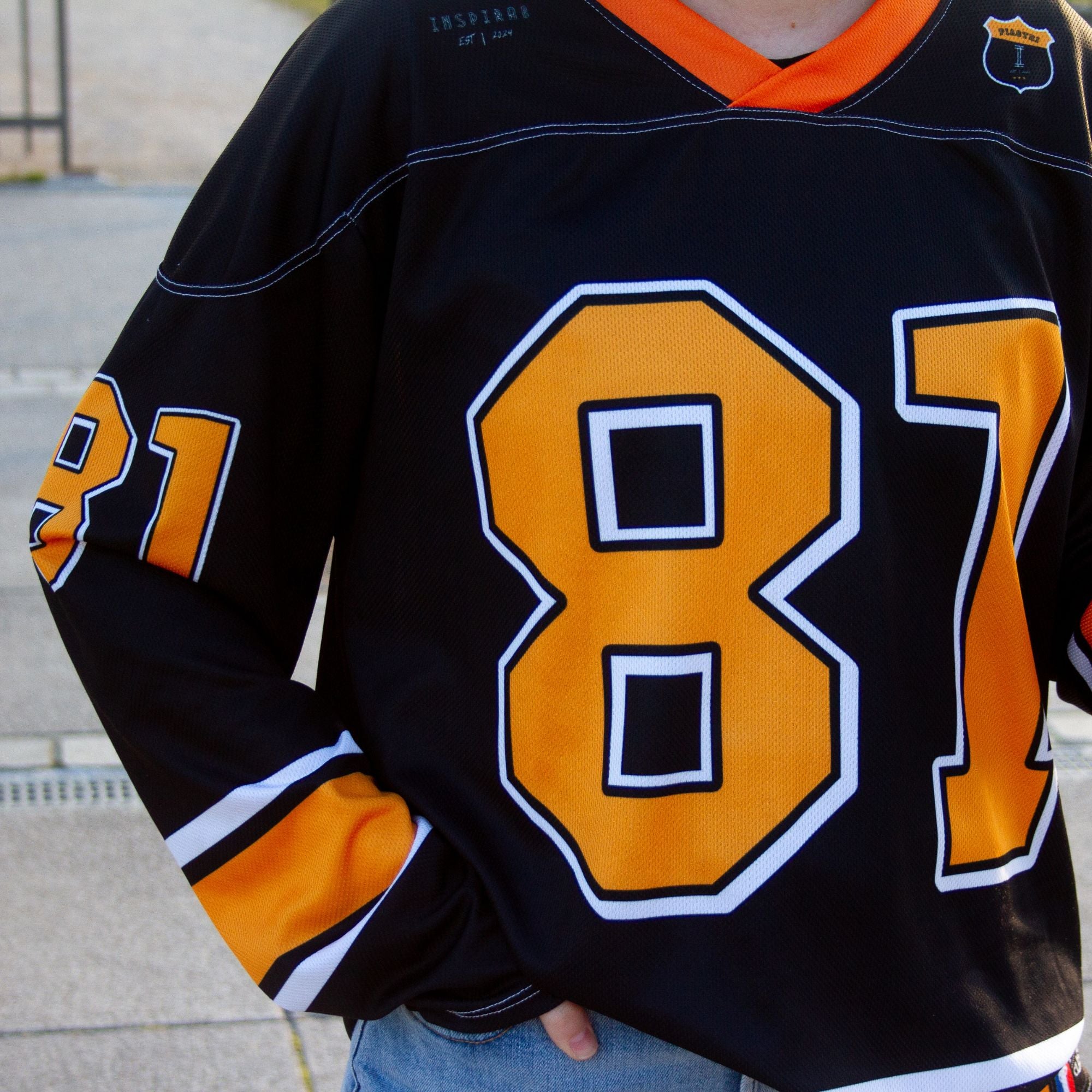 A black hockey jersey with Oscars piastri's McLaren F1 racing number 81 on the front and back in papaya orange, also the name Piastri is on the back in orange