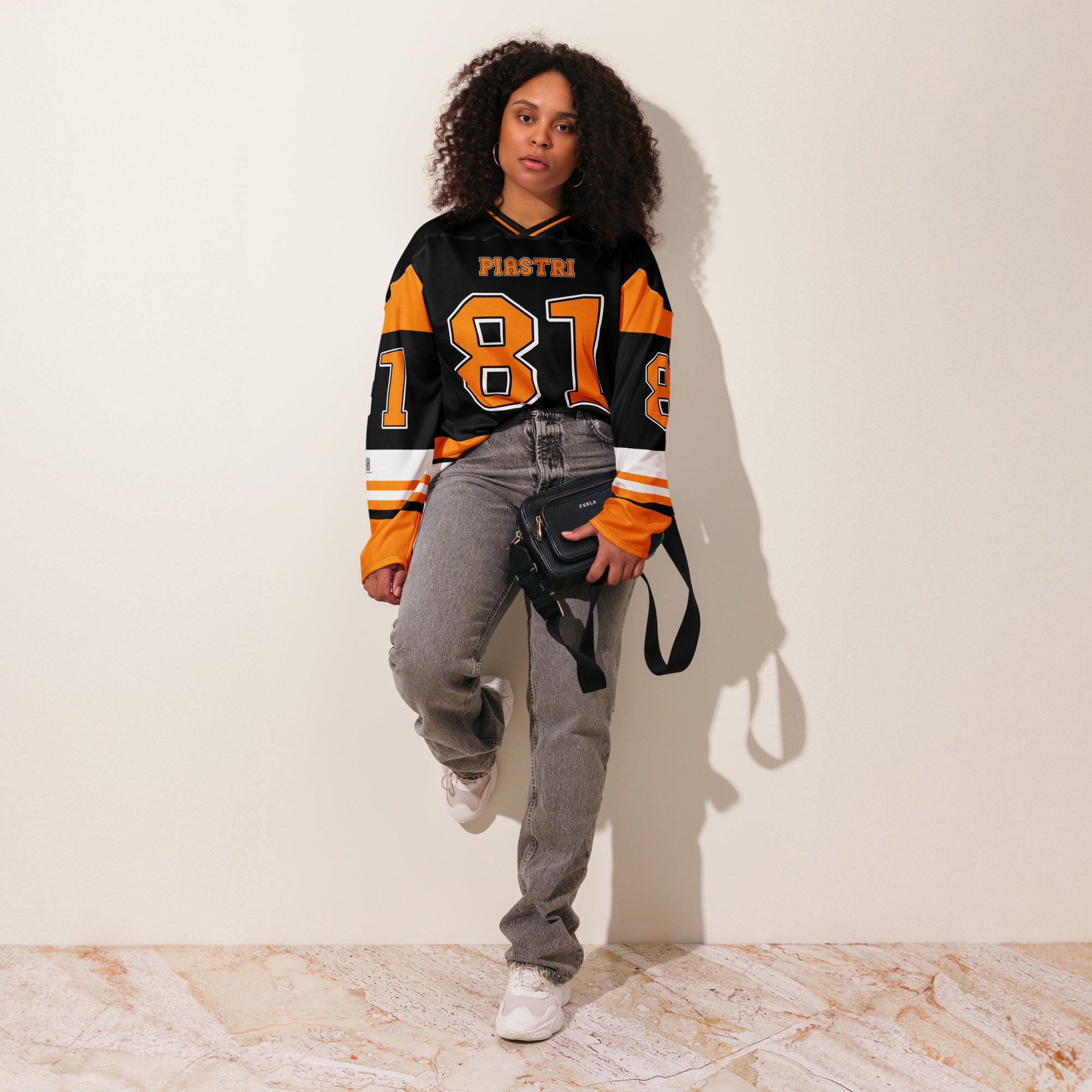 A black hockey jersey with Osacr Piastri's mclaren F1 racing number 81 on the front and back in papaya orange, also the name norris is on the back and front in orange