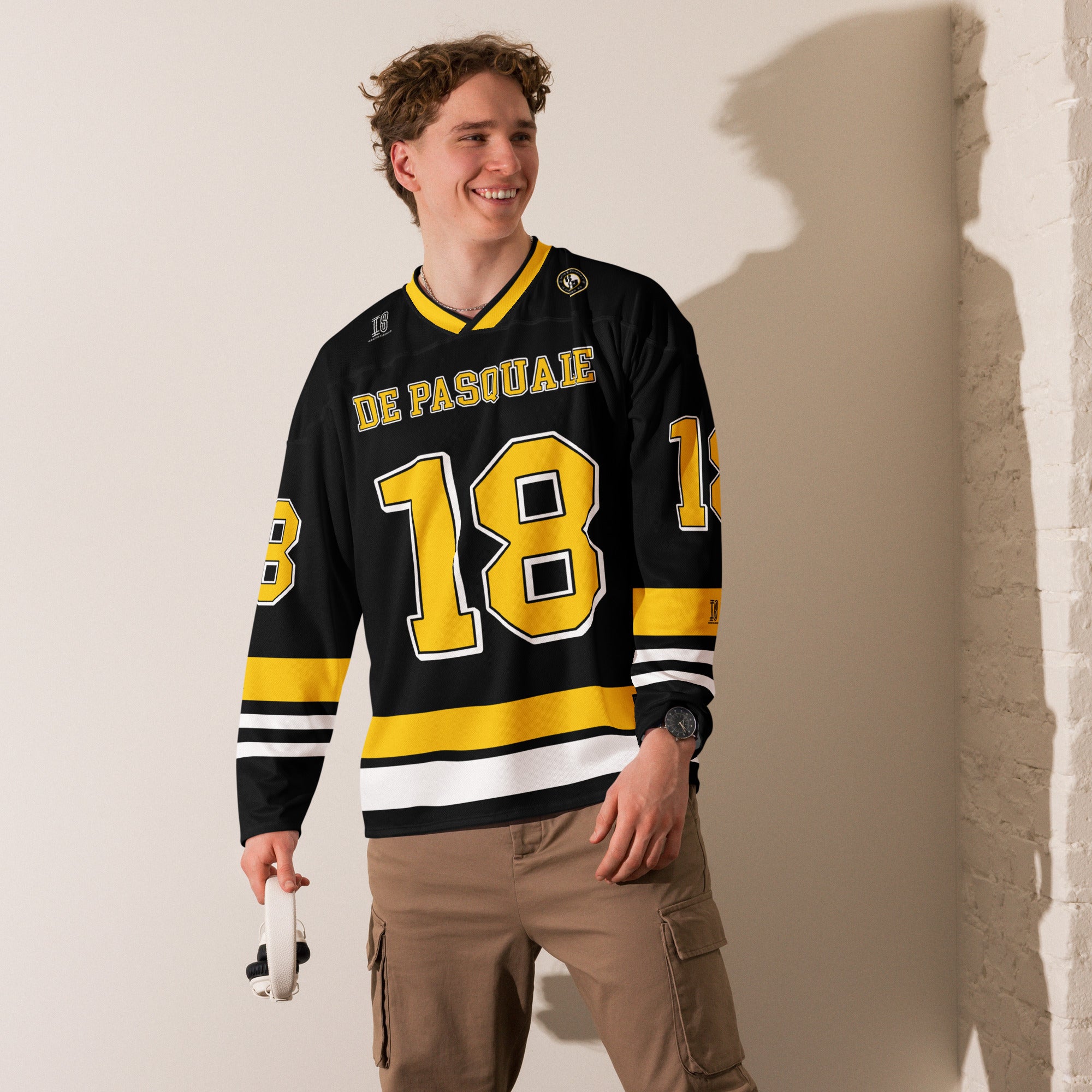 Person wearing a black hockey jersey with yellow and white details, standing against a plain wall.
