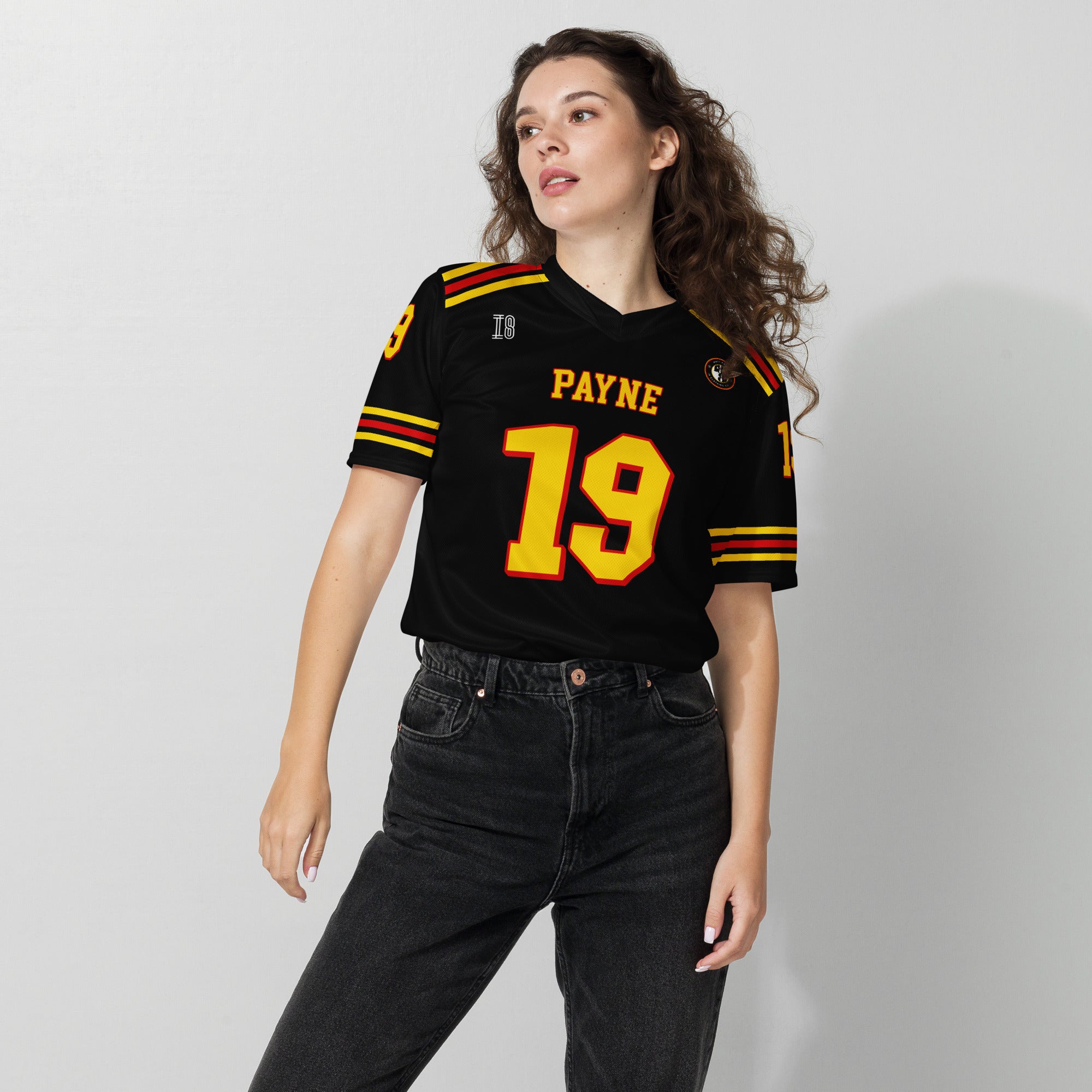 Woman wearing a black sports jersey with yellow and red details on a plain background