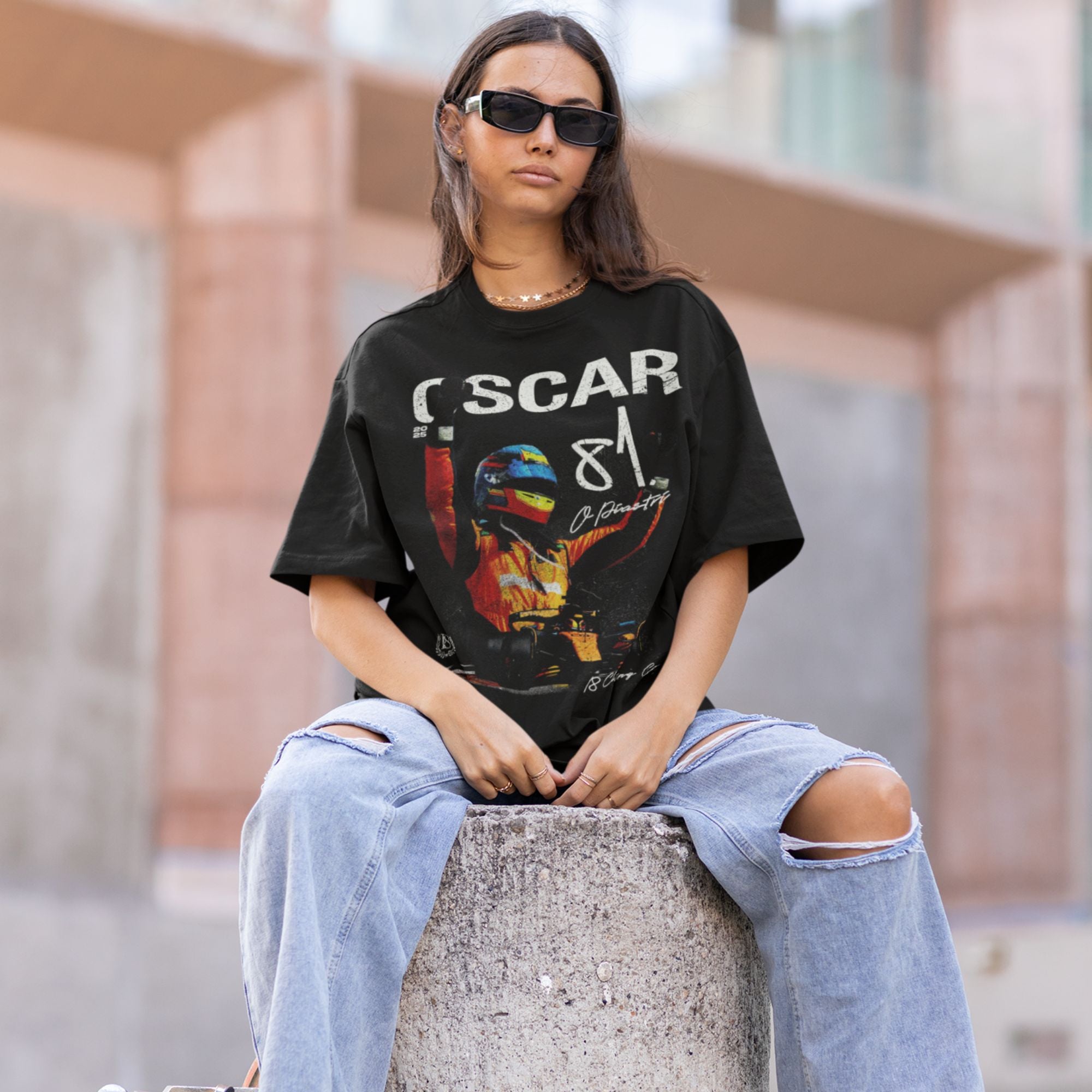 Person wearing a black t-shirt with 'Oscar 81' design, sitting on a concrete block.