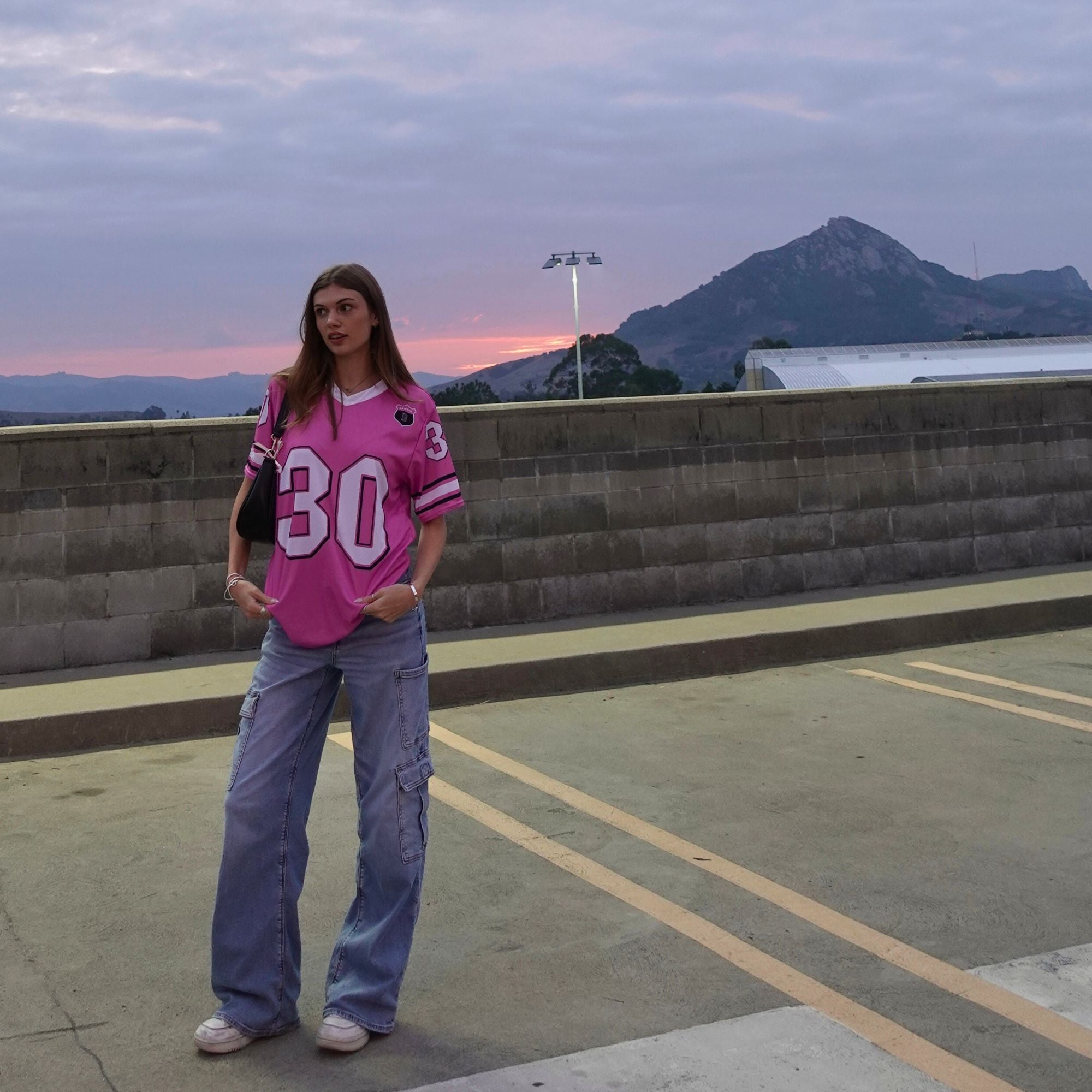 Person wearing a pink jersey with the number 30 on a rooftop at sunset.