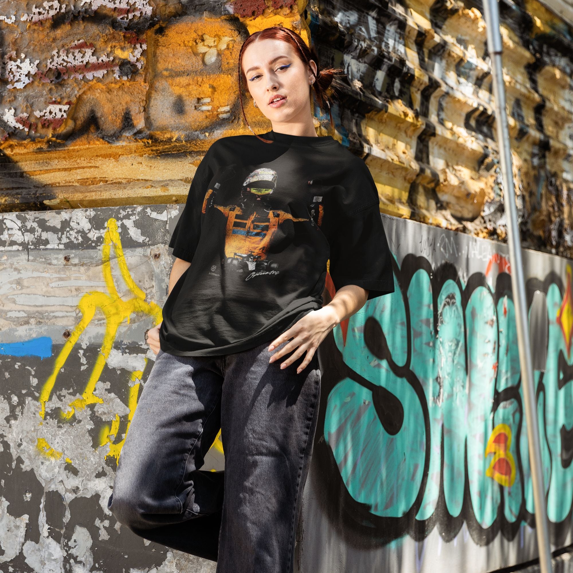 Person wearing a black t-shirt with a graphic design in front of a graffiti-covered wall.