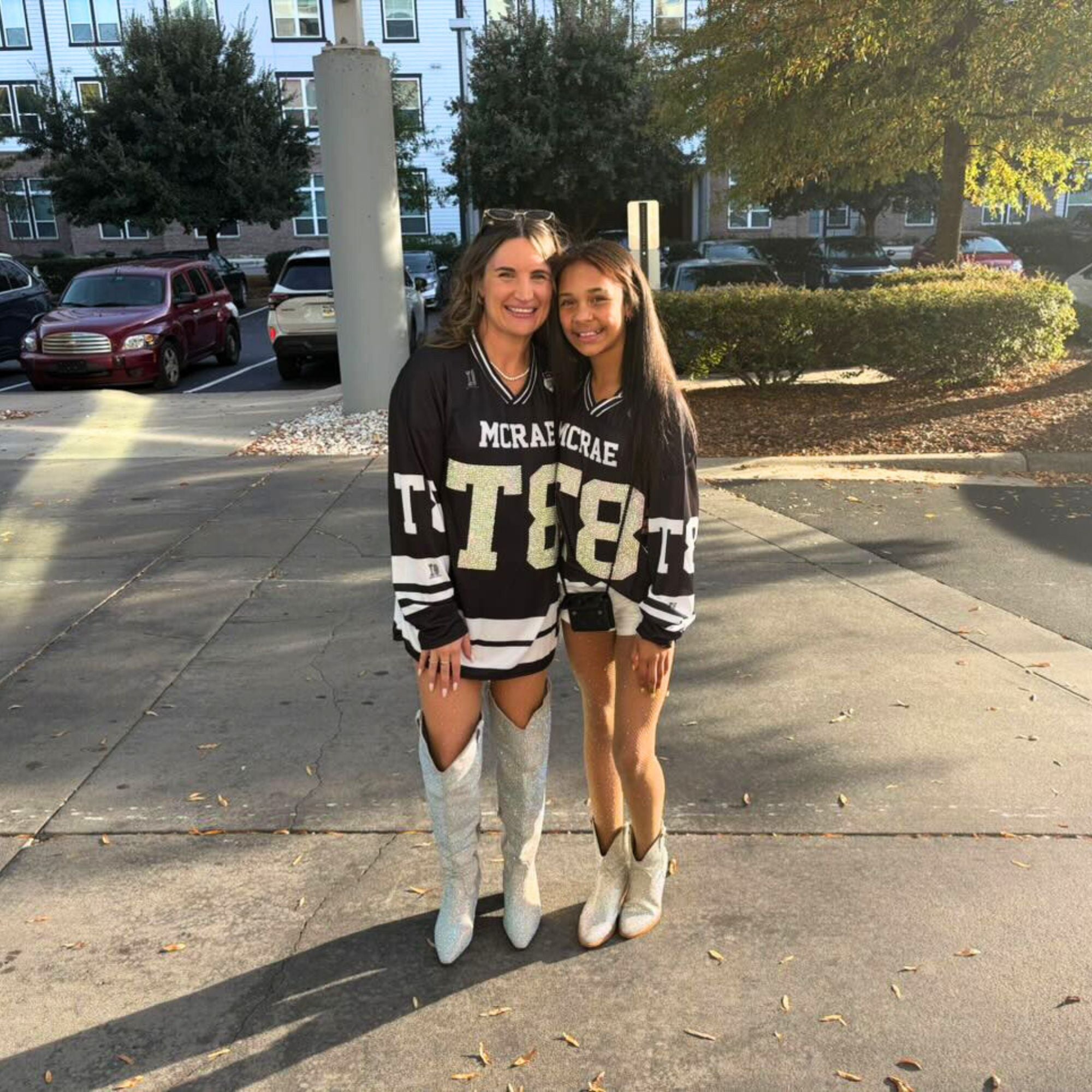Two women wearing matching sweatshirts with text on a sidewalk.
