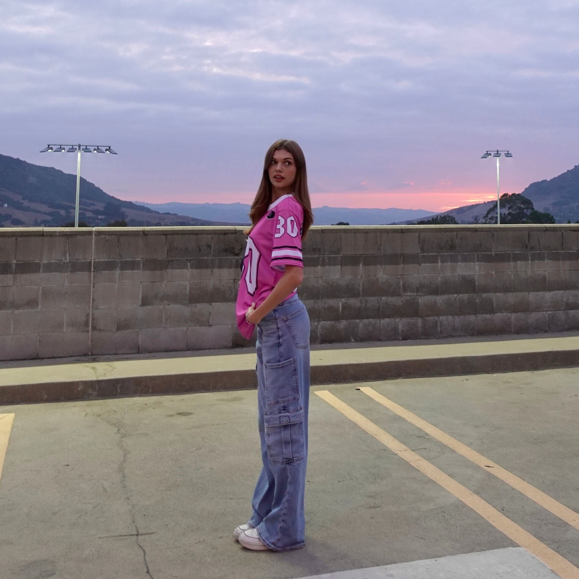 Person wearing a pink jersey with the number 30 standing on a rooftop with mountains in the background.