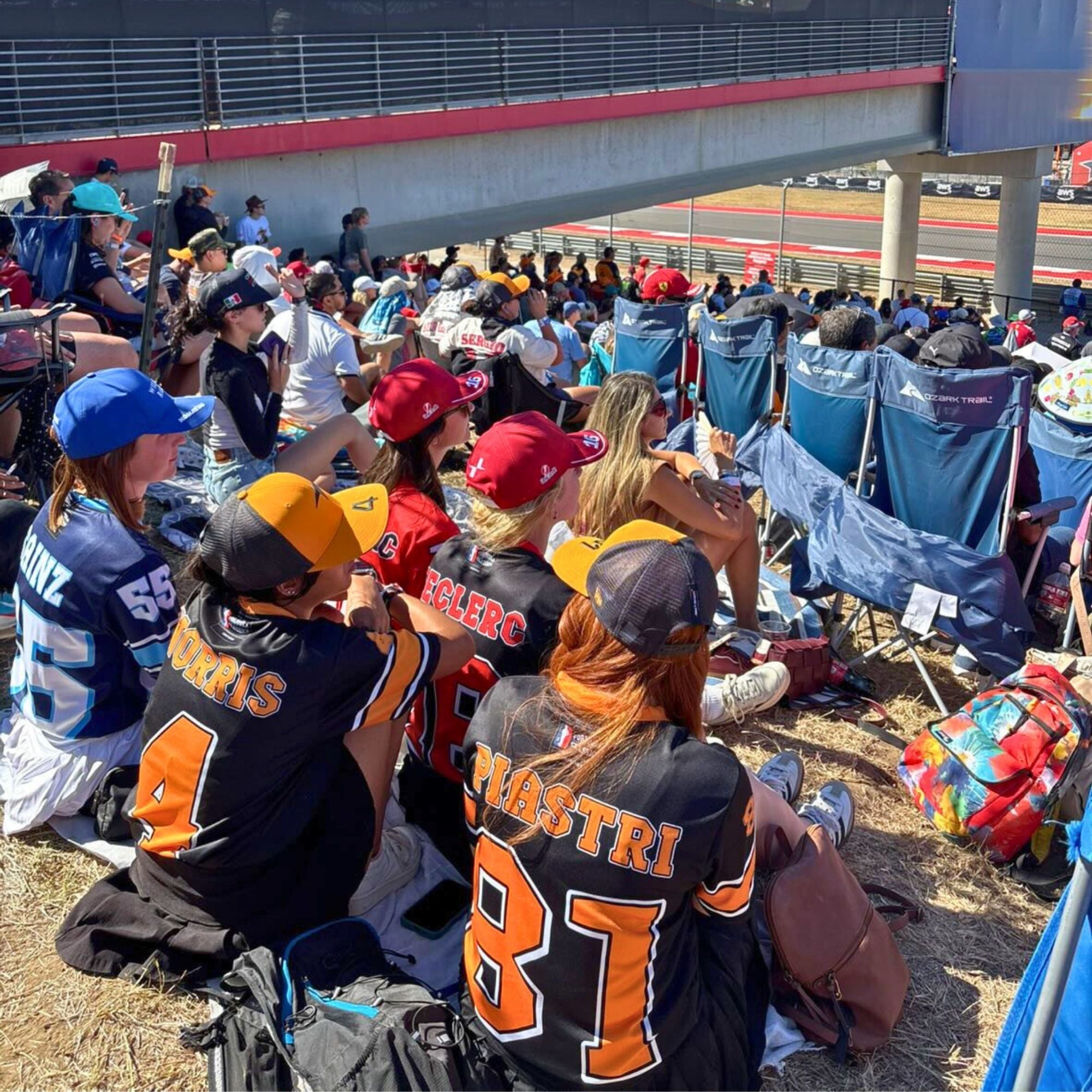 People sitting in chairs at a race track, some wearing sports jerseys.