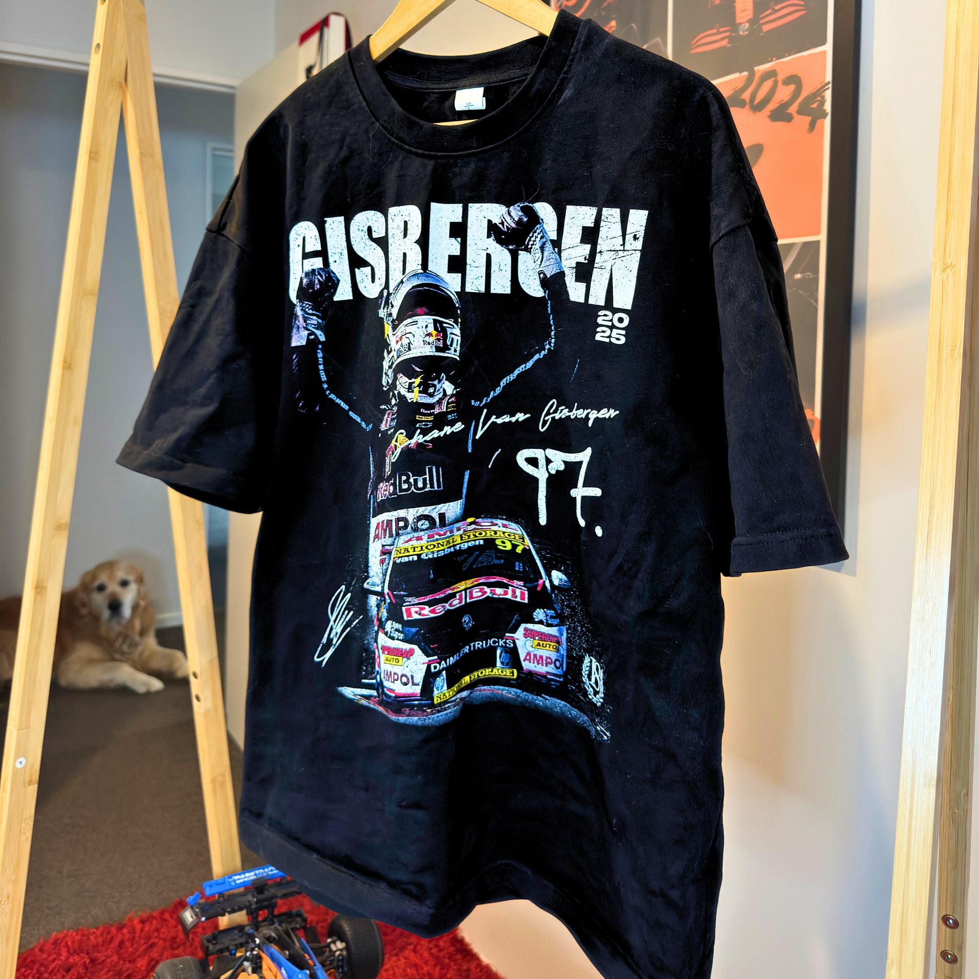 Black t-shirt with racing-themed design and text, hanging on a wooden rack.