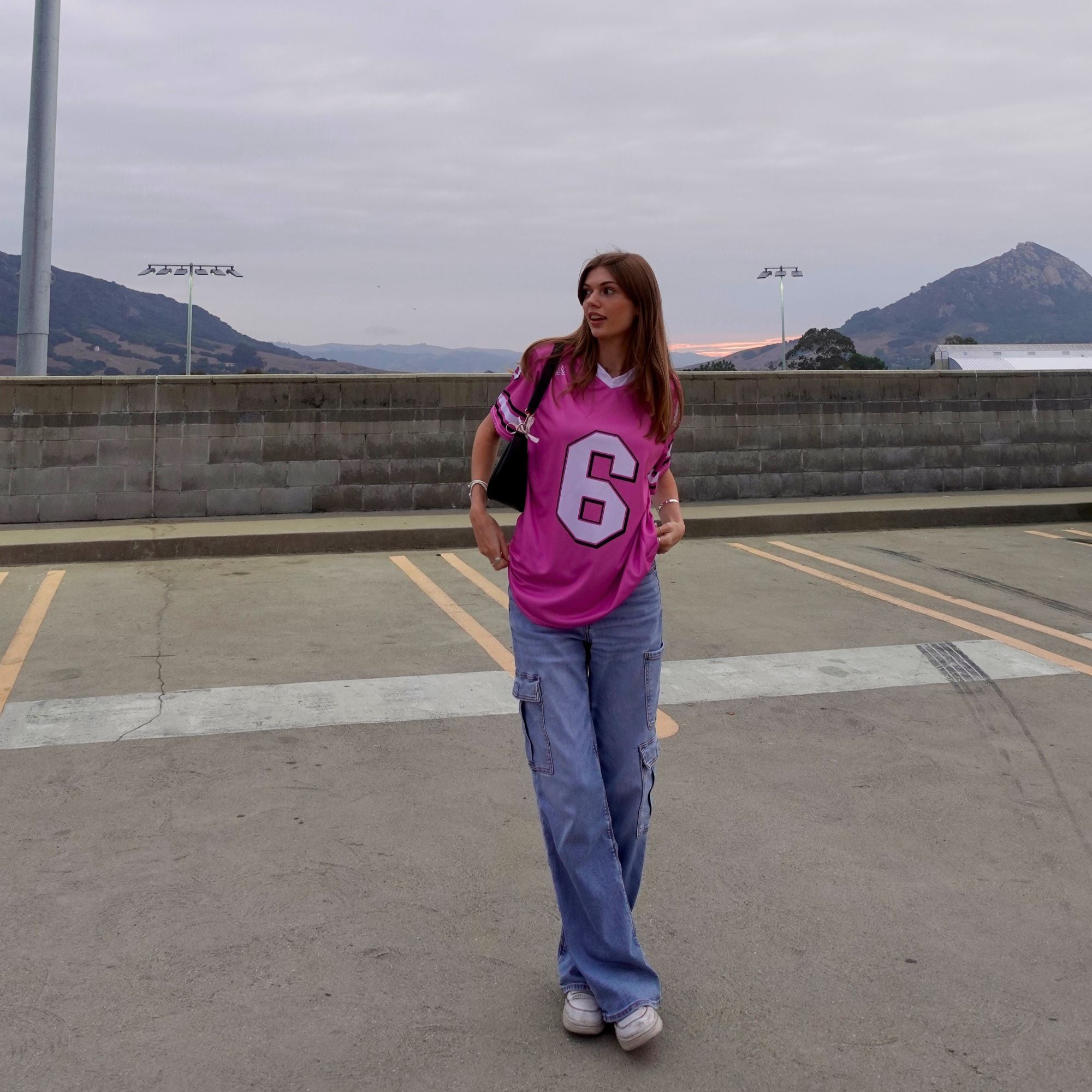 Person wearing a pink jersey with the number 6, standing on a rooftop with mountains in the background.