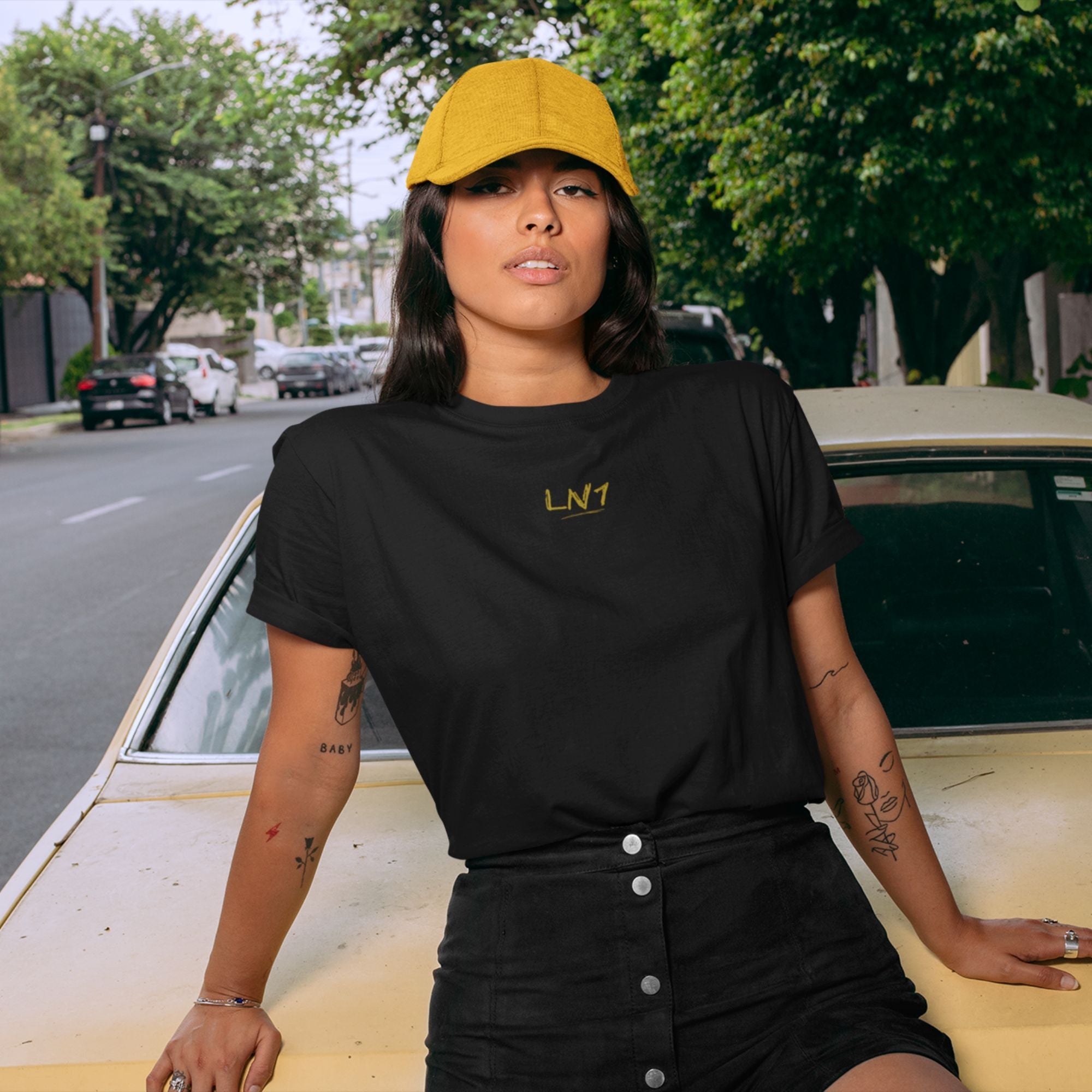 Person wearing a black t-shirt with 'LNT' logo and yellow cap, sitting on a car.