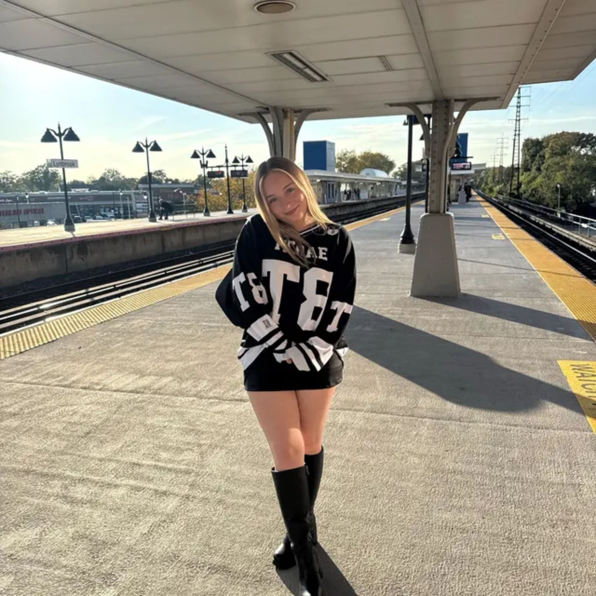 Person wearing a black sweater with white text at a train station platform