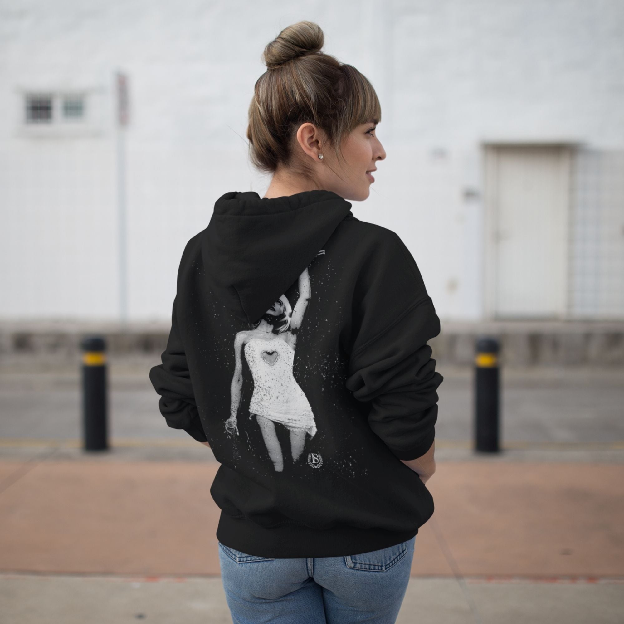 Person wearing a black hoodie with a graphic design on the back, standing outdoors.