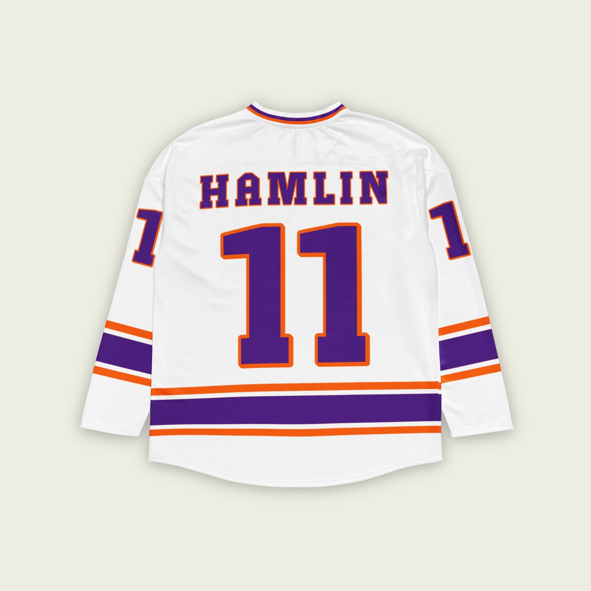 A white hockey jersey with three stripes at the bottom, the middle line is purple and other two are orange. There is Denny Hamlin's nascar number 11 on the front and back in purple with a orange outline. Denny Hamlin's last name is on the back and front as well.