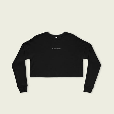 Black long-sleeve crop top with 'IN CLOTHING CO' text on a beige background