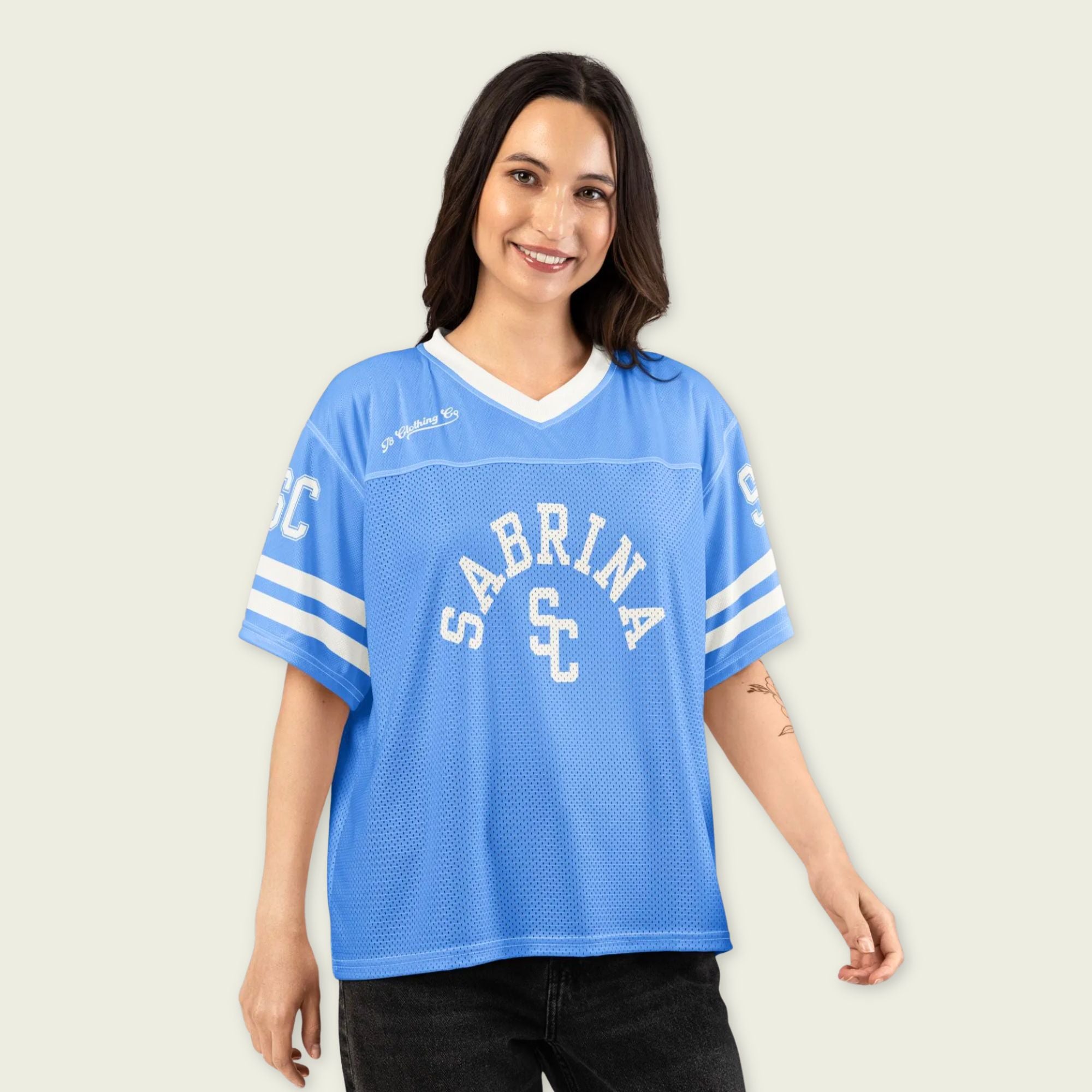 Woman wearing a blue sports jersey with 'Sabrina' and 'SC' printed on it against a plain background