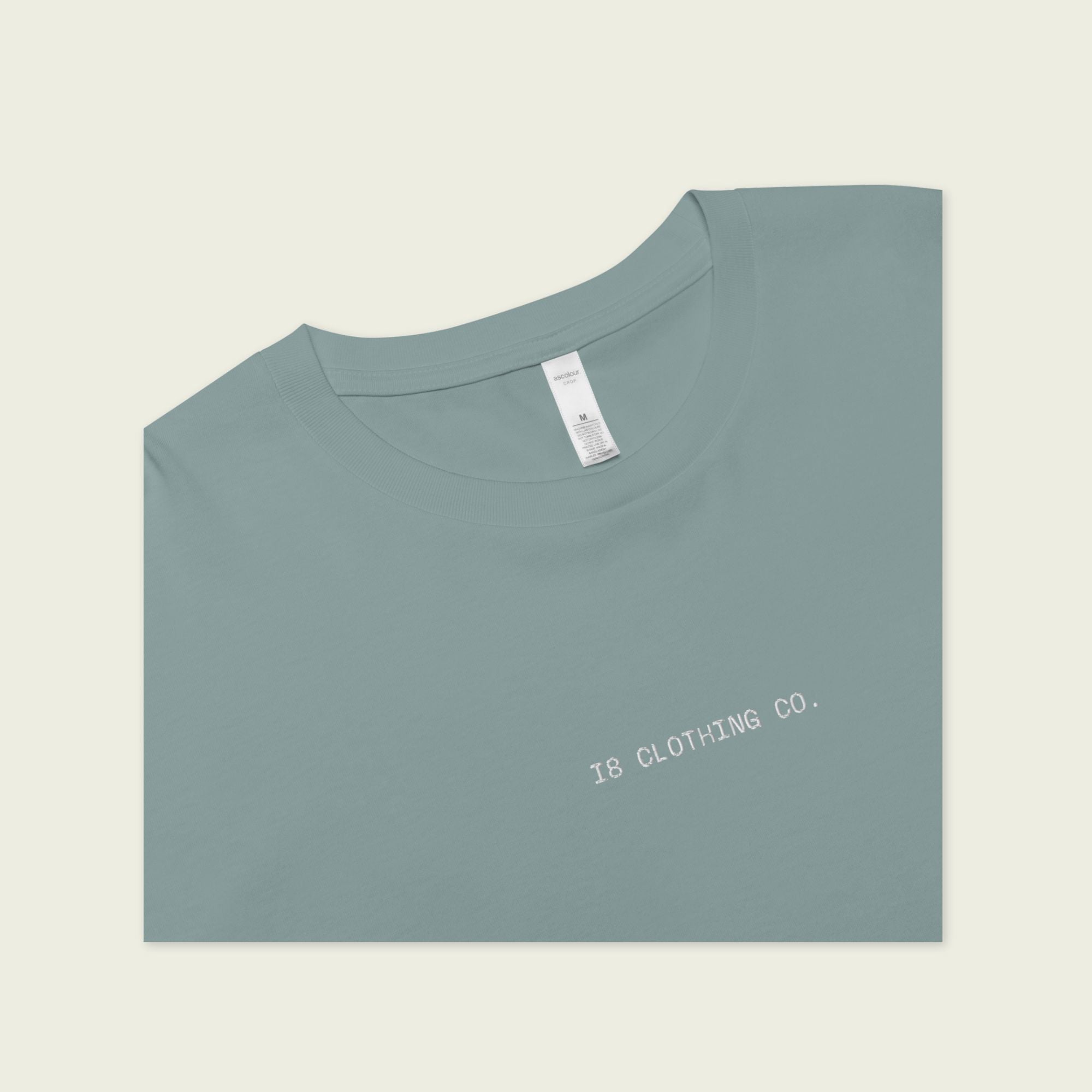 Folded light blue t-shirt with 'IS CLOTHING CO.' text on a beige background
