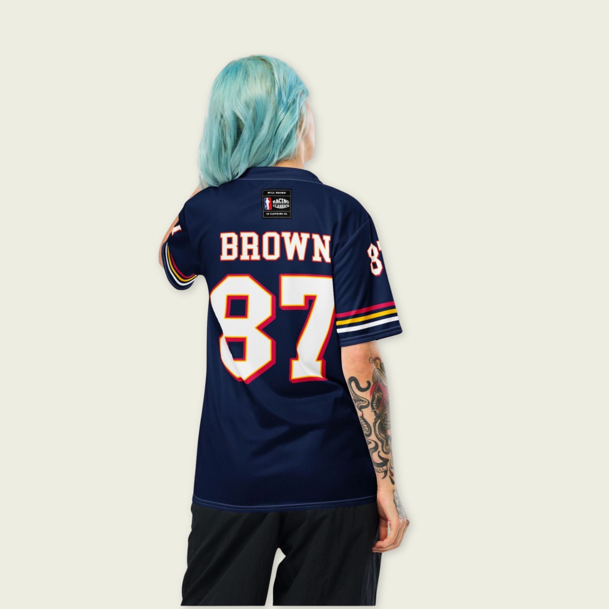 Person wearing a navy blue sports jersey with 'Brown 87' on the back, standing against a light beige background.
