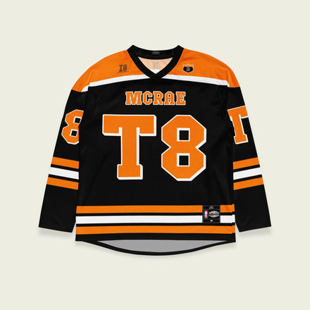 A black, orange, and white hockey jersey with the name Mcrae in orange on the front and back. Also T8 in orange on the front and back.