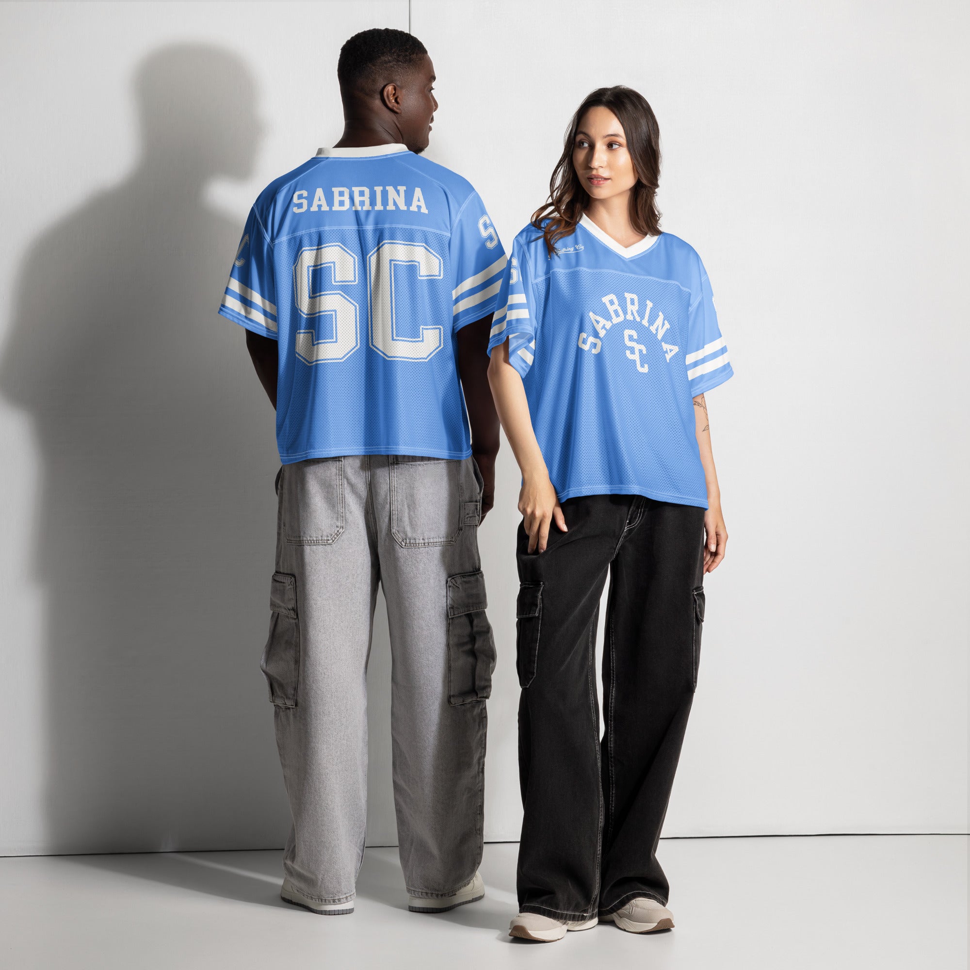 Two people wearing blue jerseys with 'Sabrina SC' text on a plain background