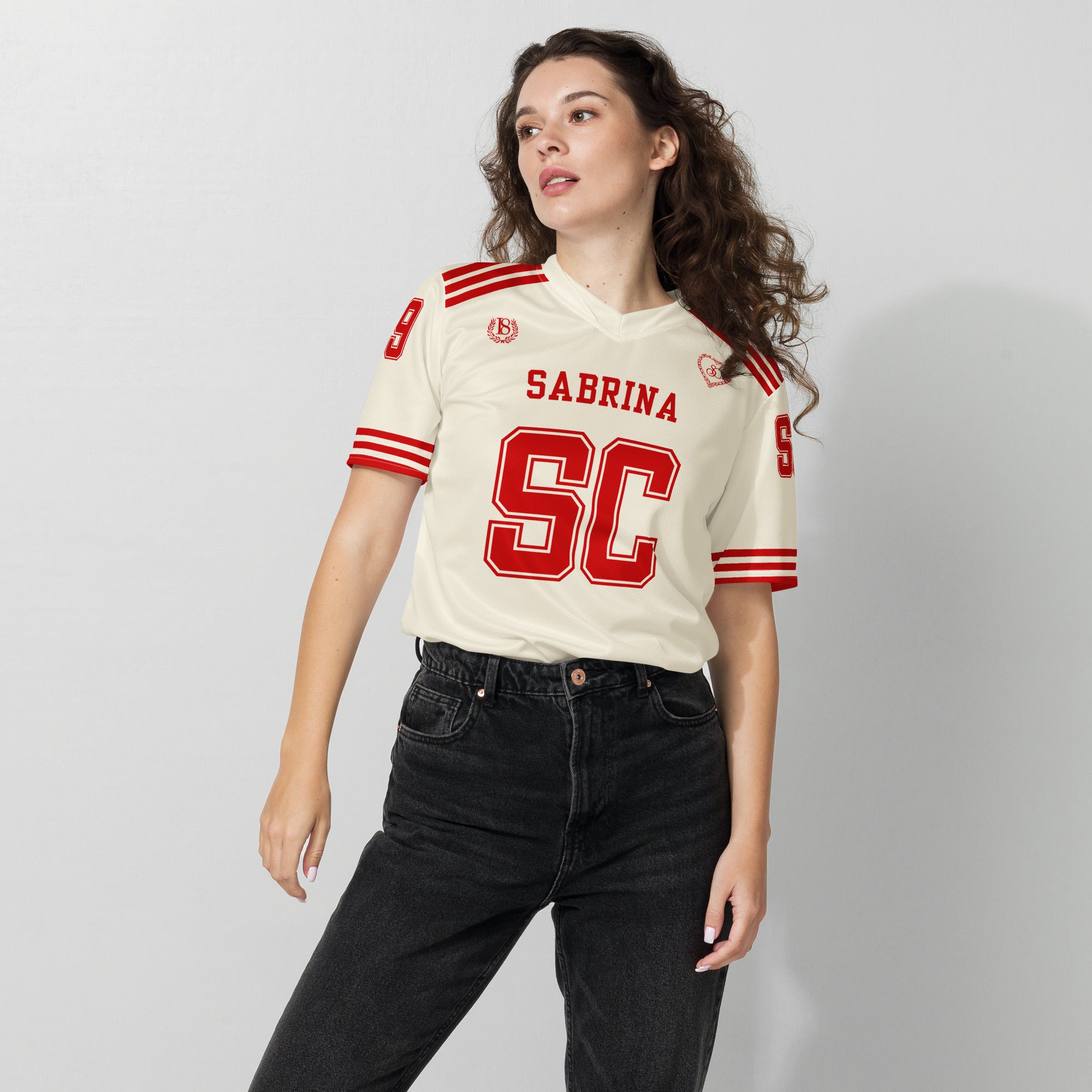 Woman wearing a cream-colored sports jersey with red lettering on a plain background